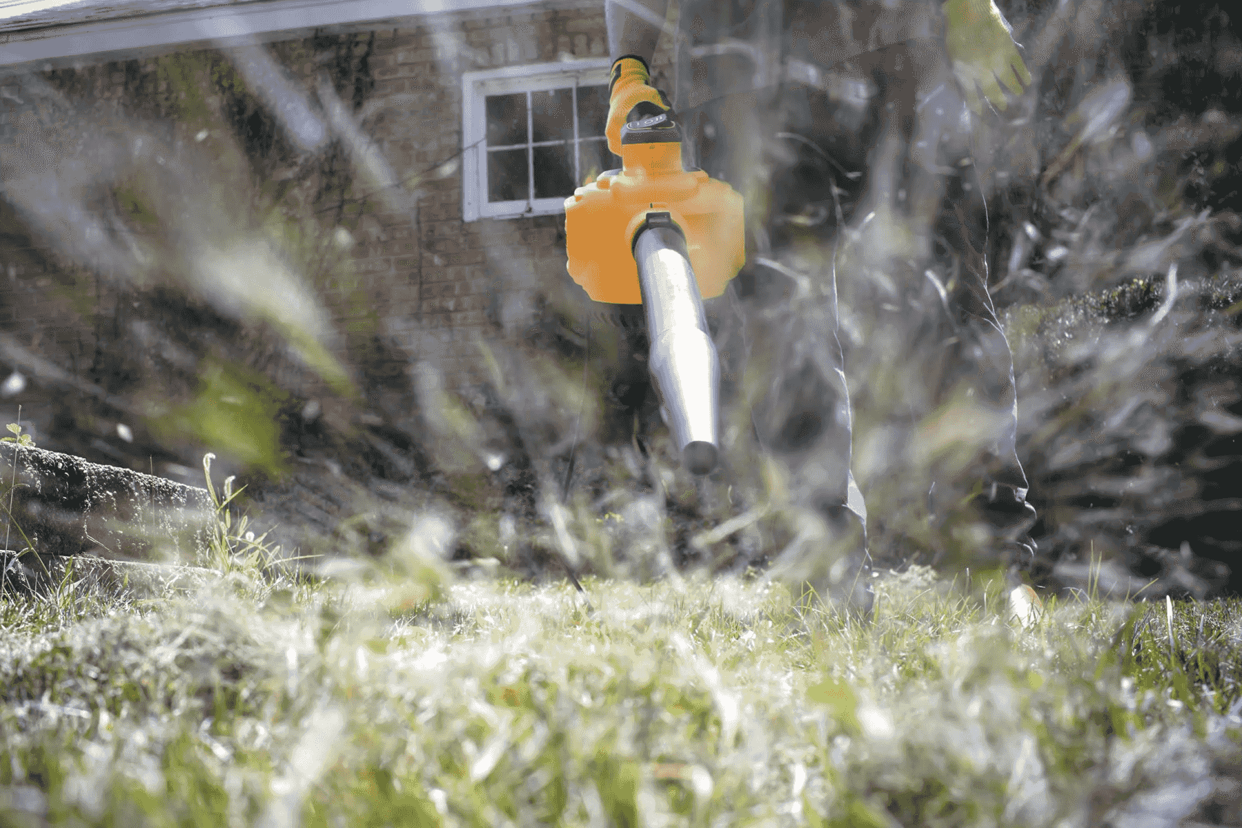 Un soffiatore per foglie giallo usato in giardino, con foglie che volano.