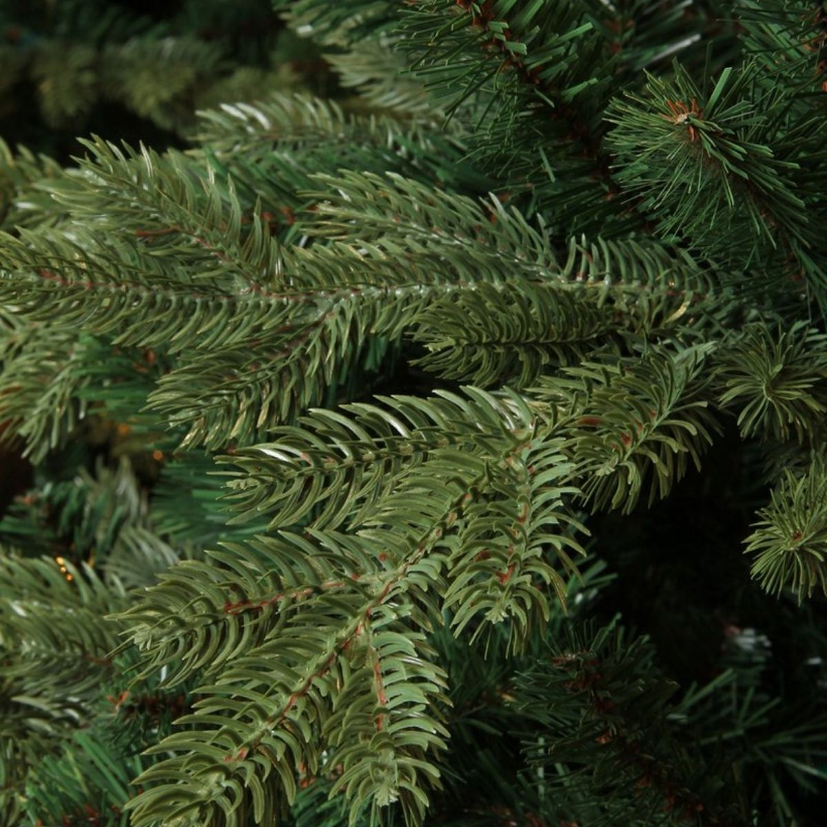 Close-up of green artificial Christmas tree branches with soft needles and brown stems.
