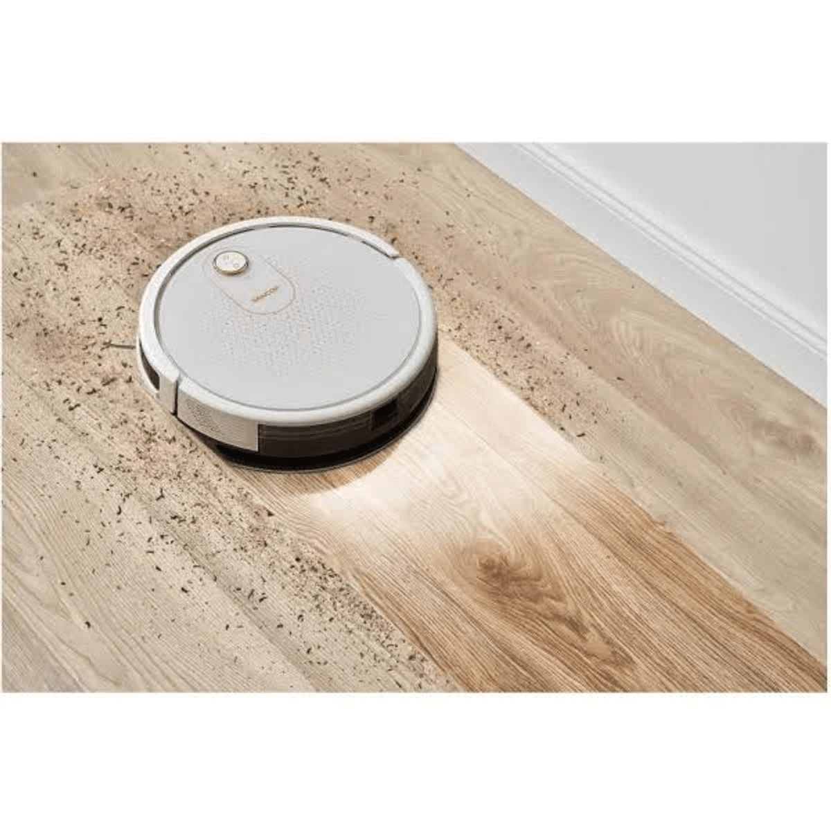 Un robot aspirapolvere bianco pulisce un pavimento in legno sporco, lasciando una scia pulita.