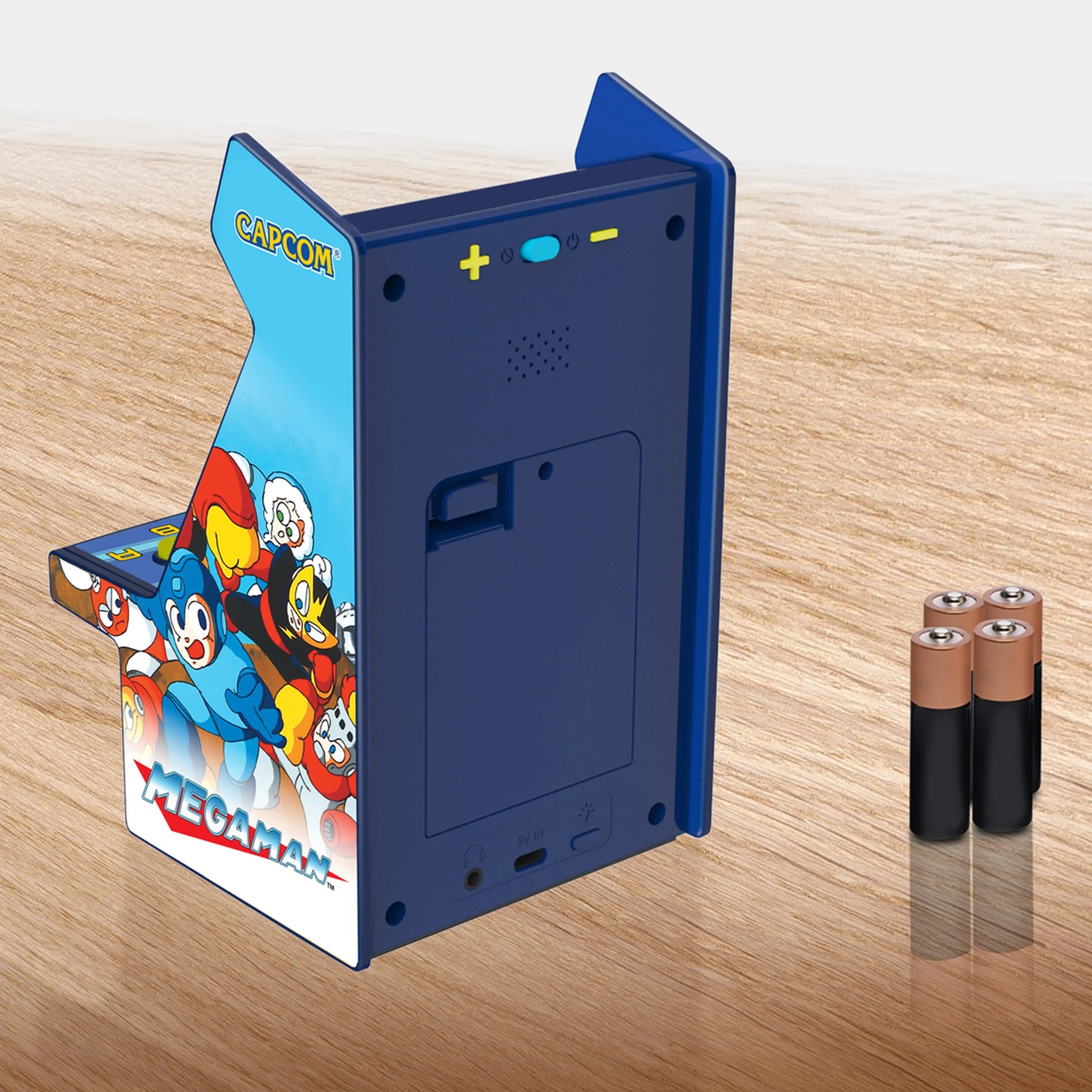 Mini arcade blu di Mega Man con quattro batterie AA su una superficie in legno.