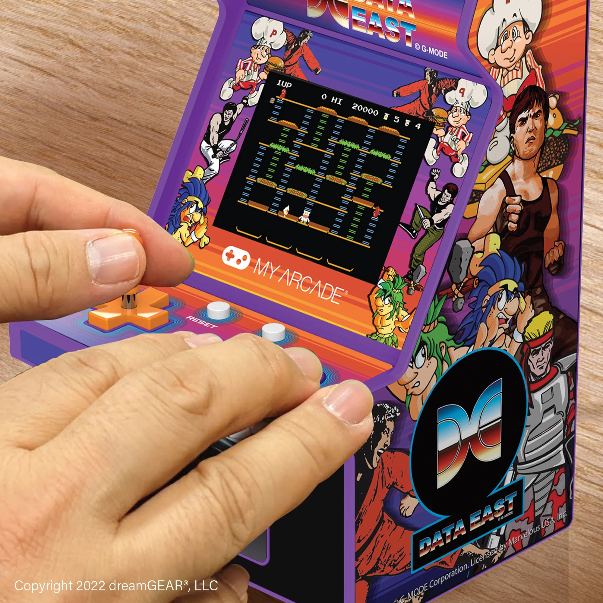 Eine Person spielt an einem violetten Data East My Arcade-Mini-Spielautomaten auf Holzuntergrund.