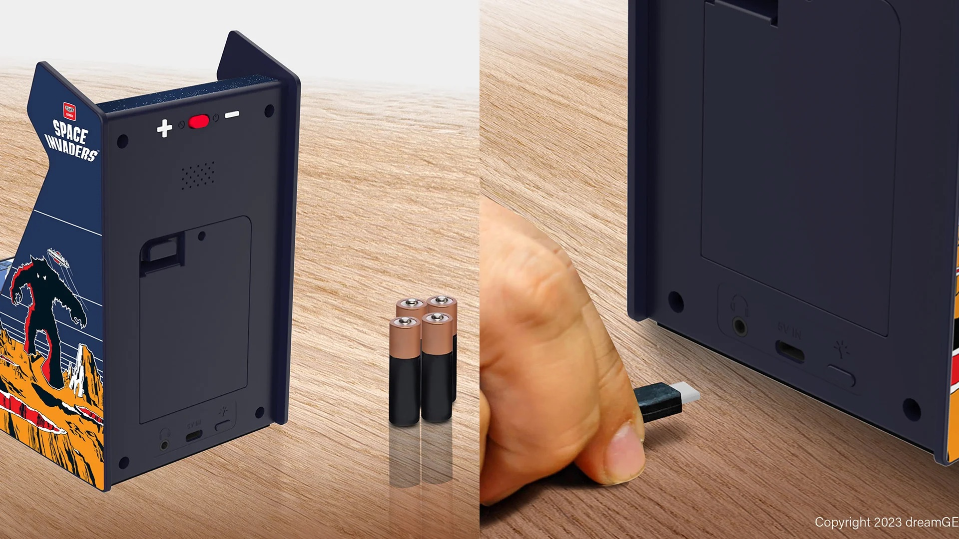 Mini cabinato arcade Space Invaders su tavolo in legno, con quattro batterie e una mano che collega un cavo USB.
