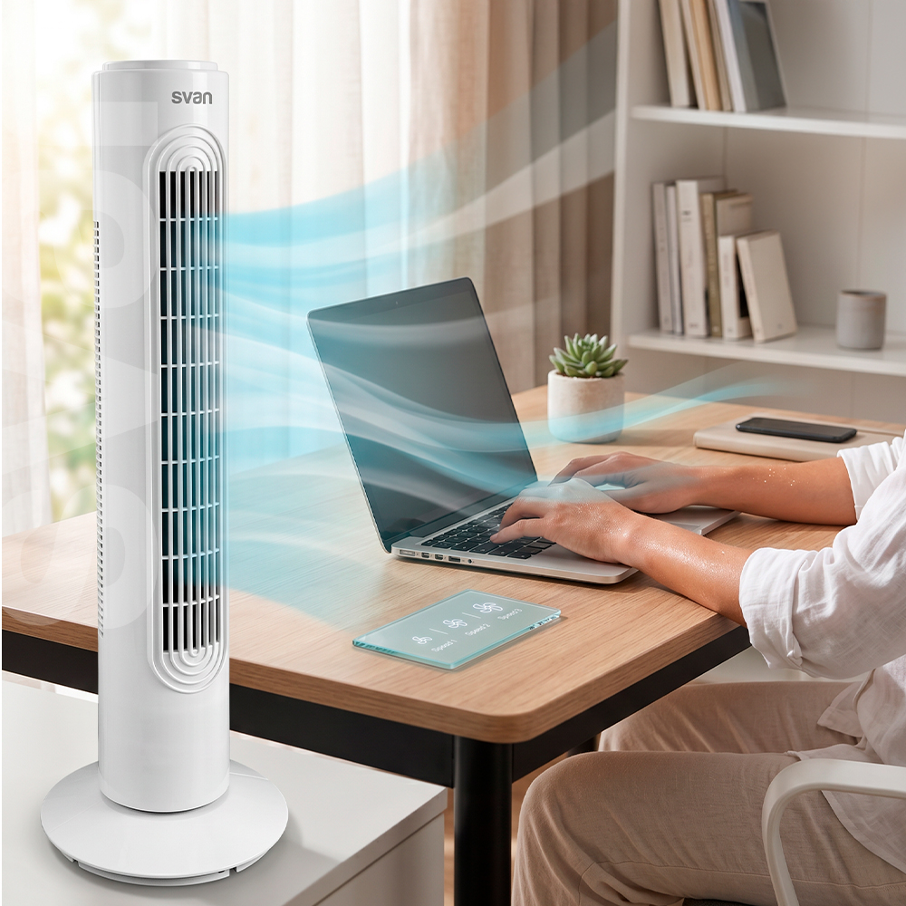 Un ventilador de torre blanco en un escritorio sopla aire fresco hacia una persona con un portátil.