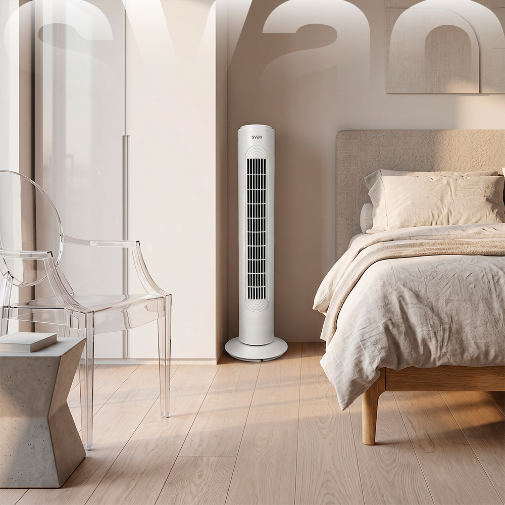 Un ventilador de torre blanco se encuentra en un dormitorio luminoso junto a una cama y una silla transparente.