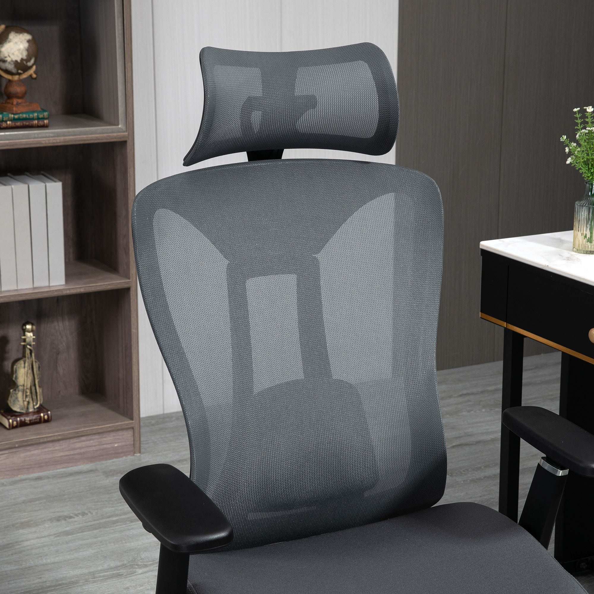 Una silla de oficina de malla gris se encuentra en una habitación moderna con una estantería y un escritorio al fondo.
