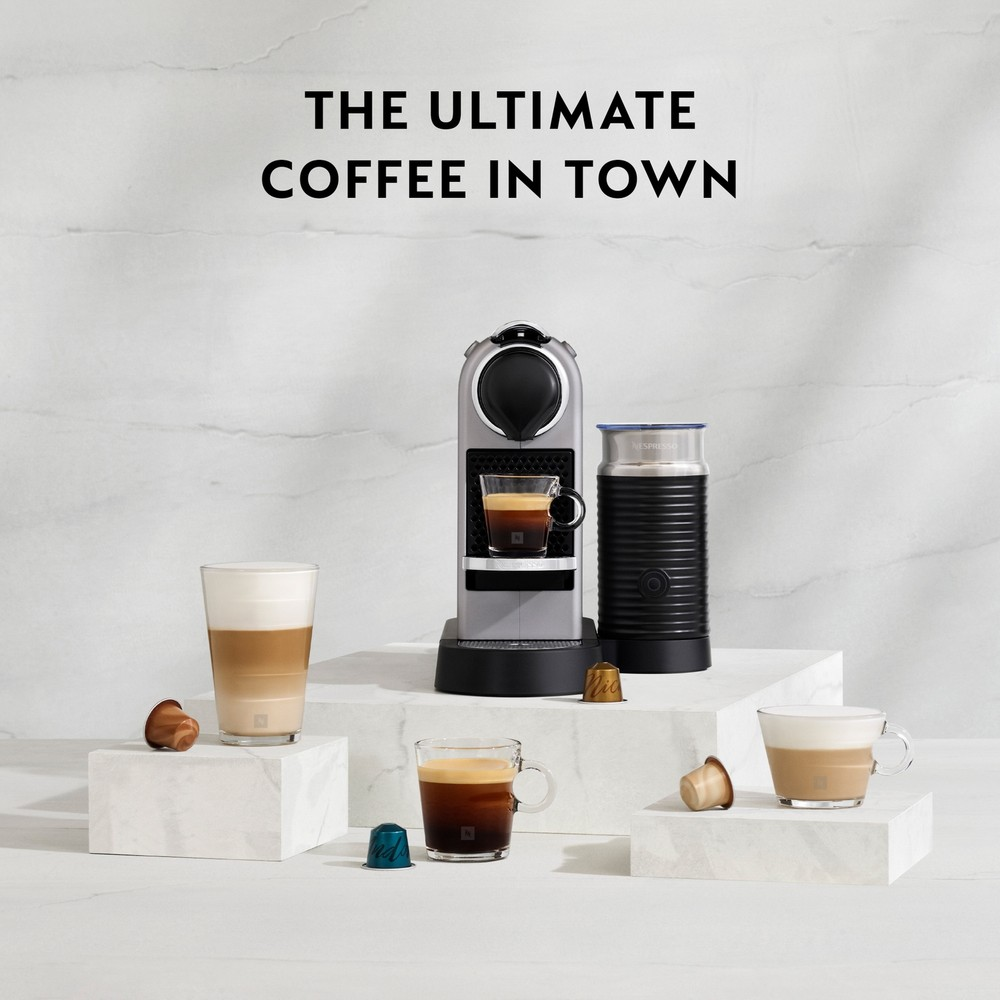 Beyaz duvar önünde mermer bloklar üzerinde Nespresso makinesi, süt köpürtücü ve fincanlar.