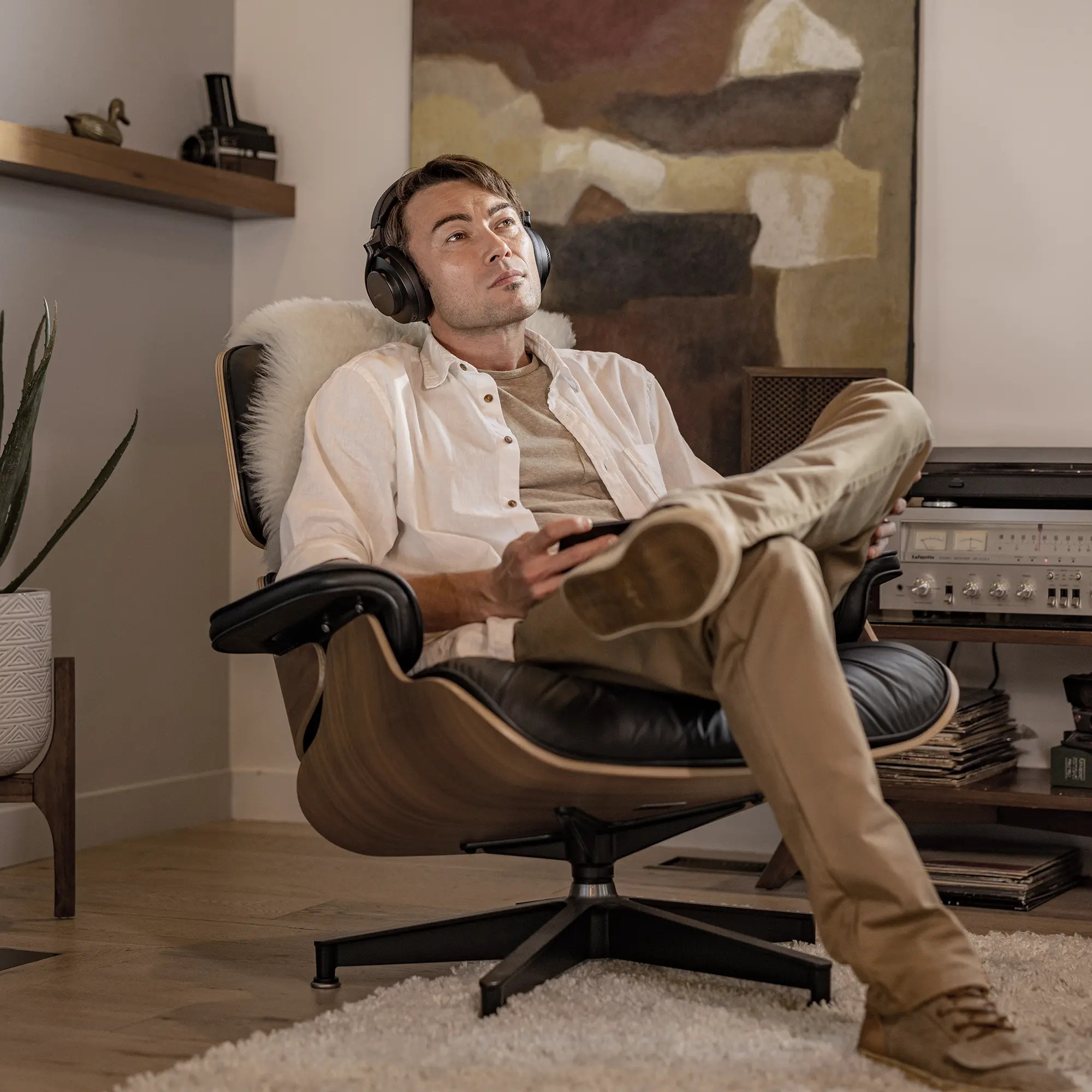 Un uomo con le cuffie si rilassa su una poltrona moderna in un soggiorno, tenendo in mano un telefono.