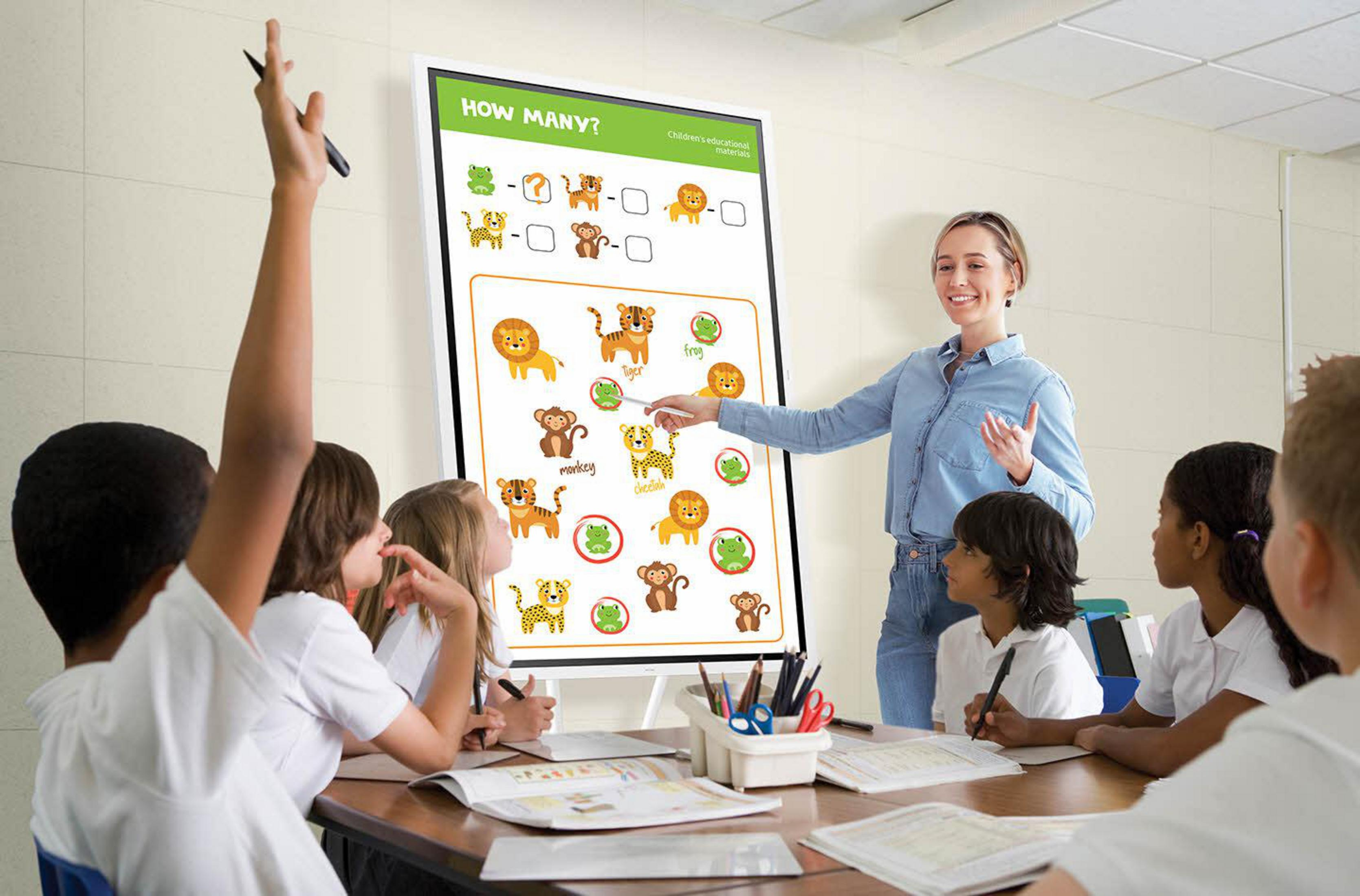 Un'insegnante indica una lavagna con disegni di animali mentre gli studenti in classe siedono e alzano la mano.