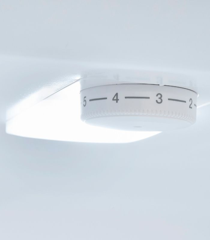 Ein weißer, runder Thermostatknopf mit den Zahlen 2 bis 5 an einer weißen Wand.