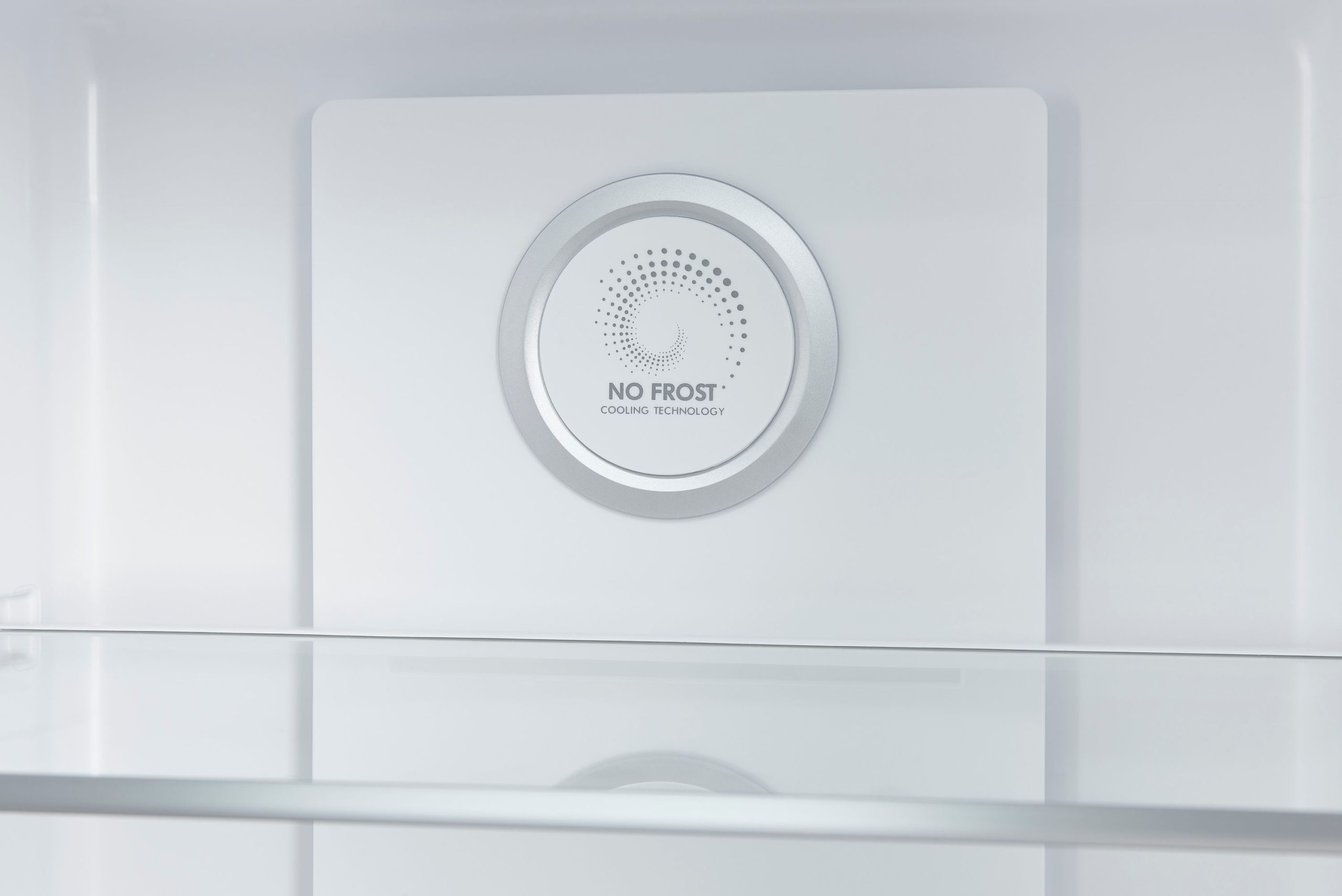 Innenraum eines Kühlschranks mit No Frost Kühltechnologie-Logo an der Wand und Glasregalen.