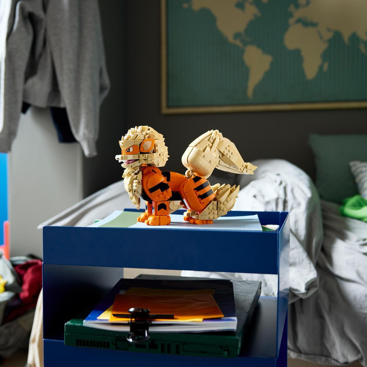 Arka planda dünya haritası olan bir yatak odasındaki mavi komodinin üzerinde Lego Arcanine oyuncağı.