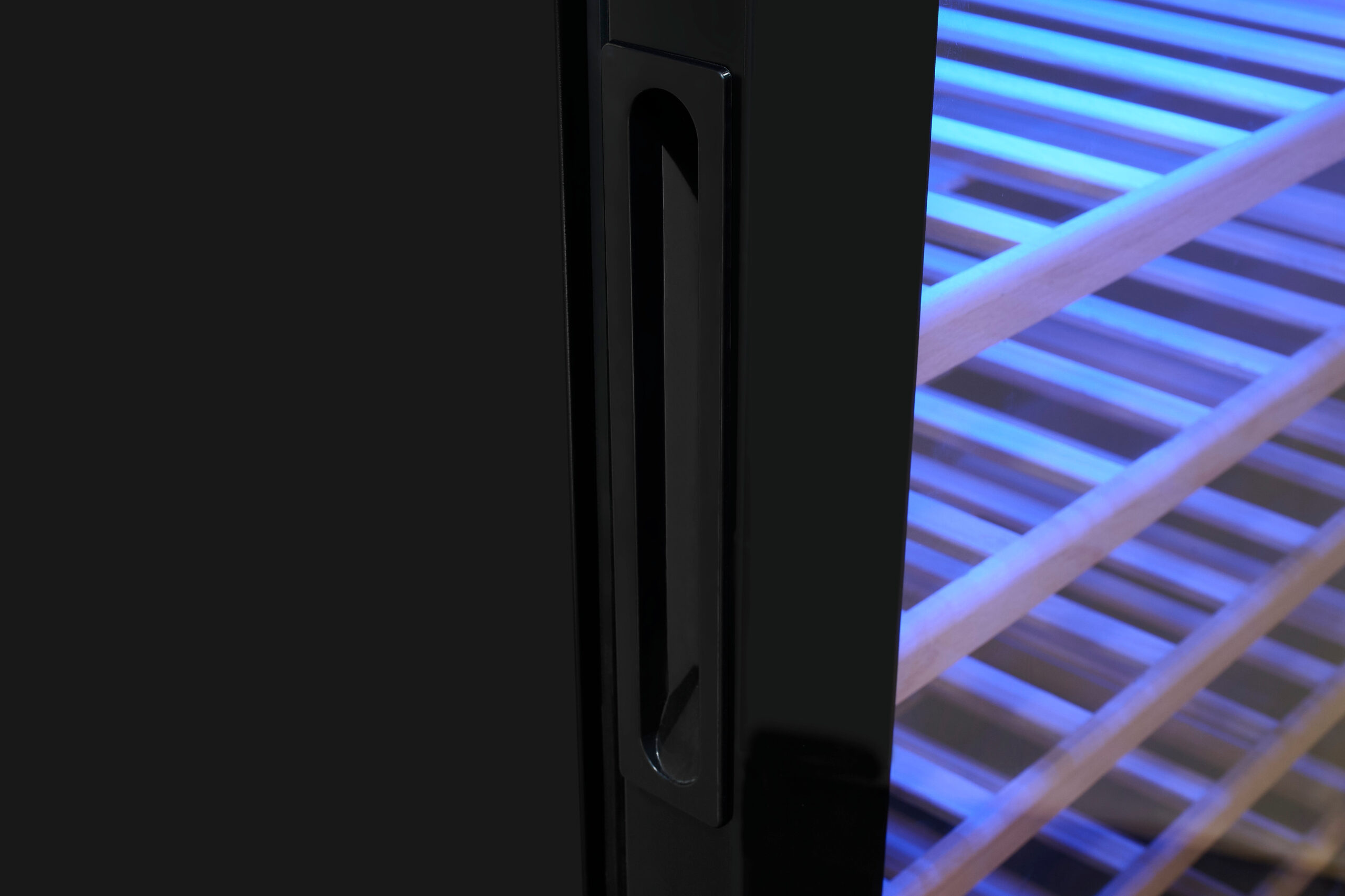 Primer plano de un tirador de enfriador de vino negro con estantes de madera iluminados por luz azul.