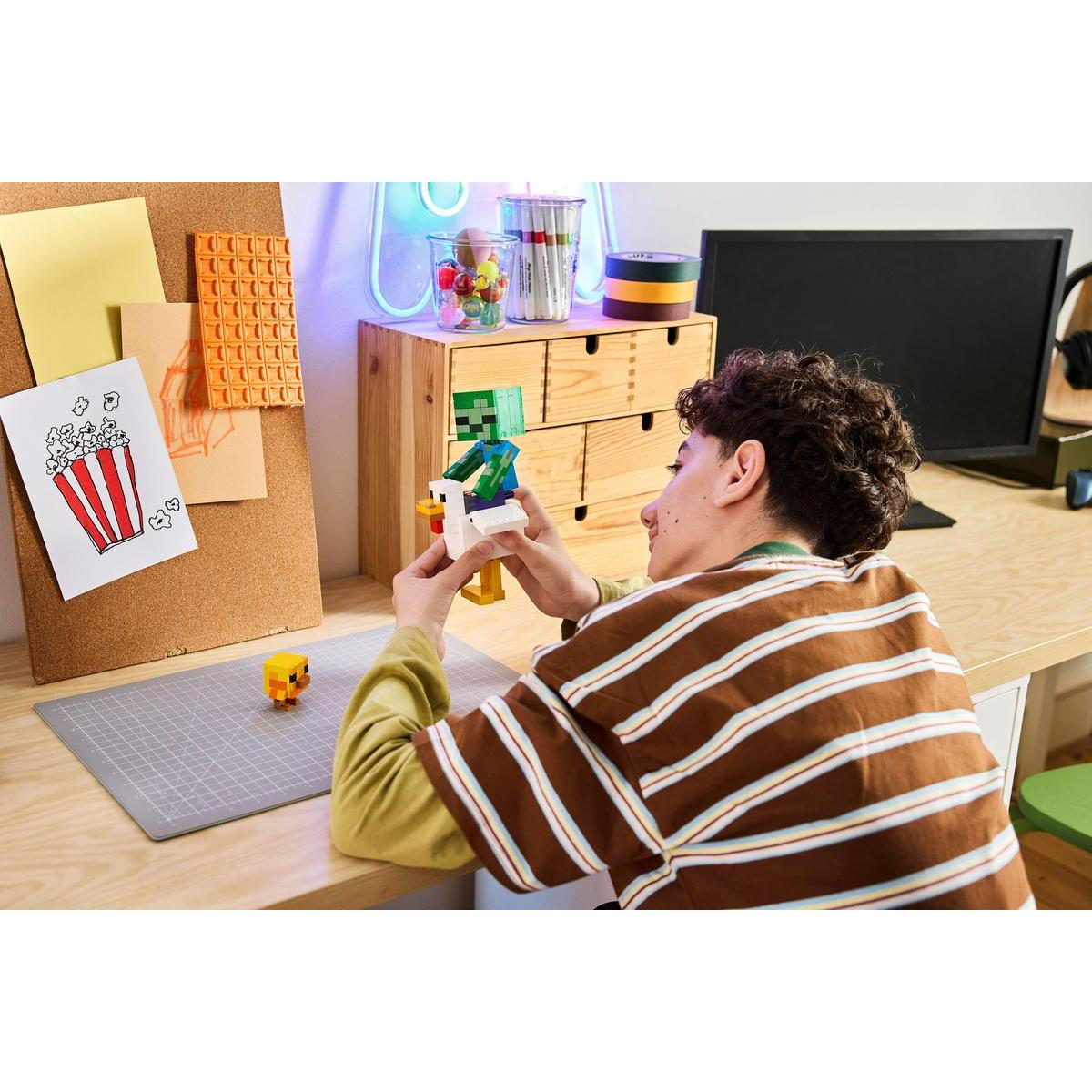 Un niño con un suéter a rayas se sienta en un escritorio construyendo un personaje de Minecraft con bloques.