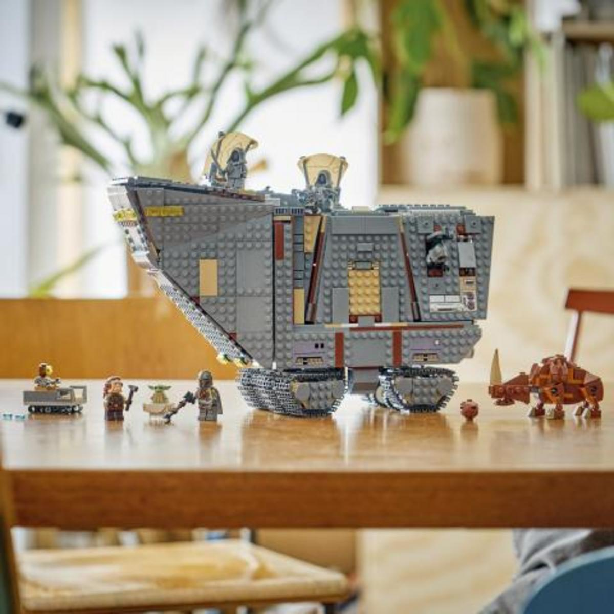 Un gran vehículo de transporte blindado Lego Star Wars gris en una mesa de madera, rodeado de minifiguras y una criatura.