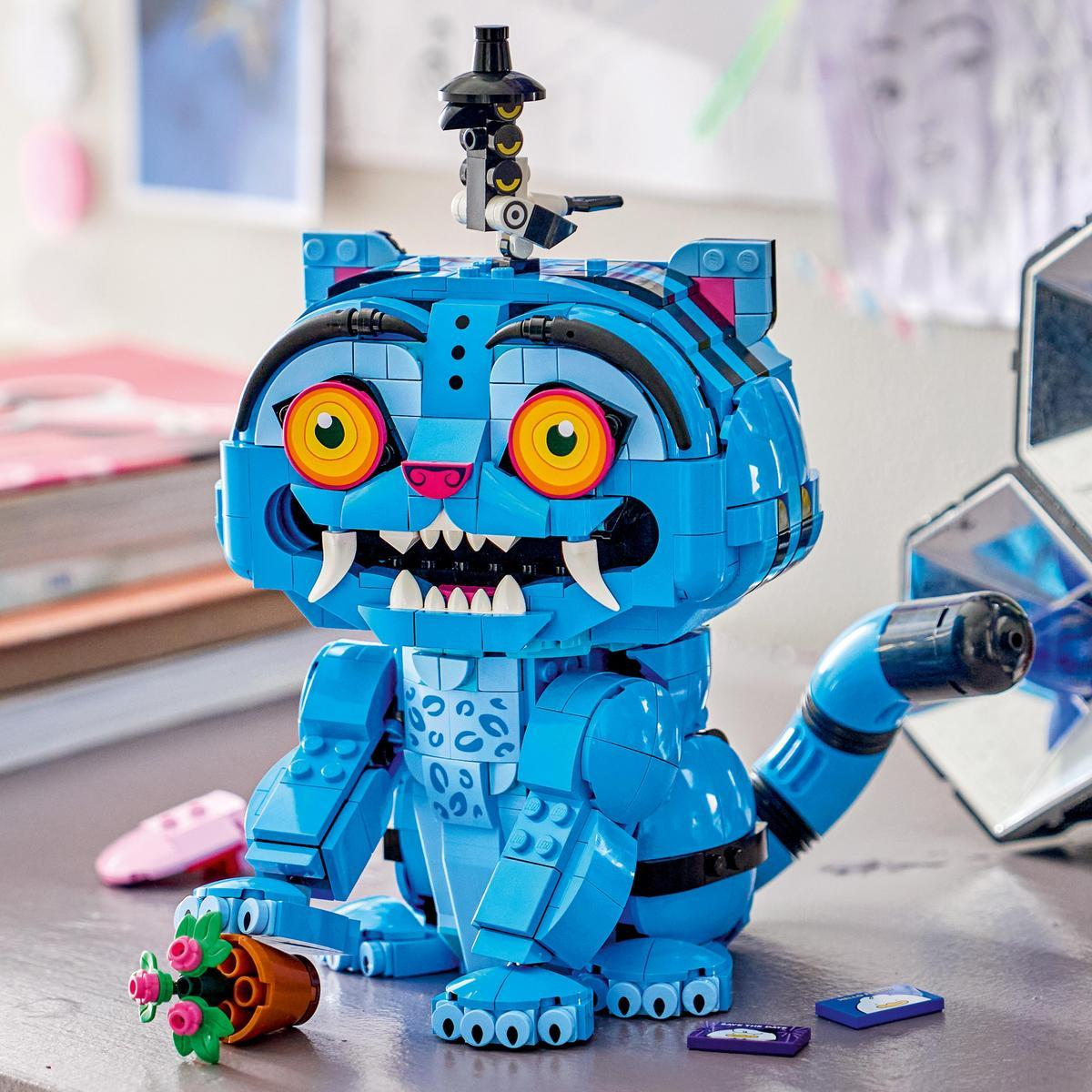 Büyük sarı gözleri, beyaz dişleri ve kafasında küçük bir kuş figürü olan mavi bir Lego kedi figürü.