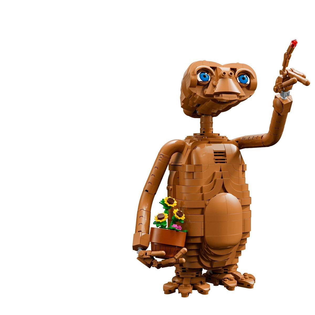 Una figura de Lego marrón de E.T. sostiene una maceta con el dedo rojo brillante levantado sobre un fondo blanco.