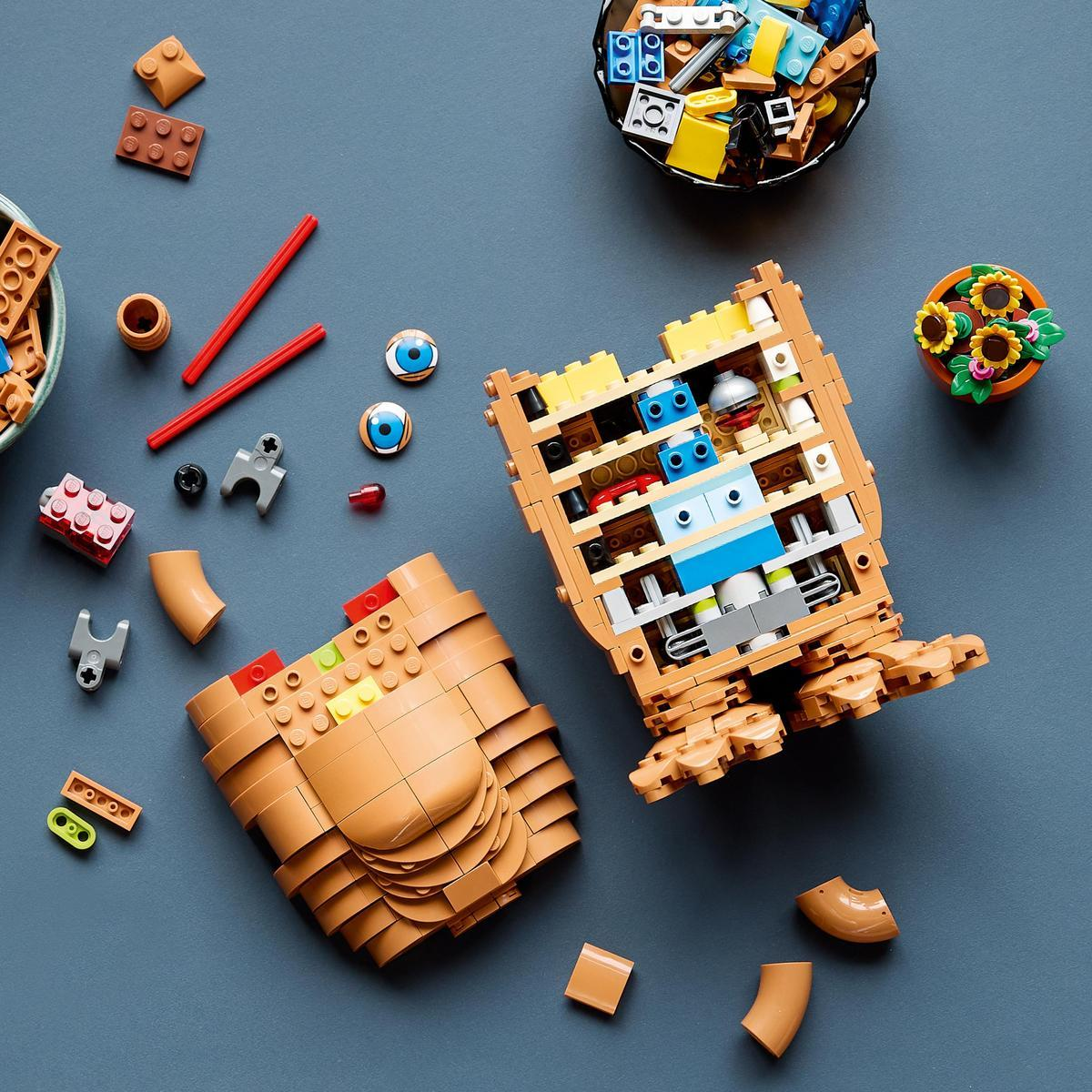 Una figura de Lego Groot parcialmente ensamblada sobre fondo azul, rodeada de piezas sueltas, cuencos y una maceta.