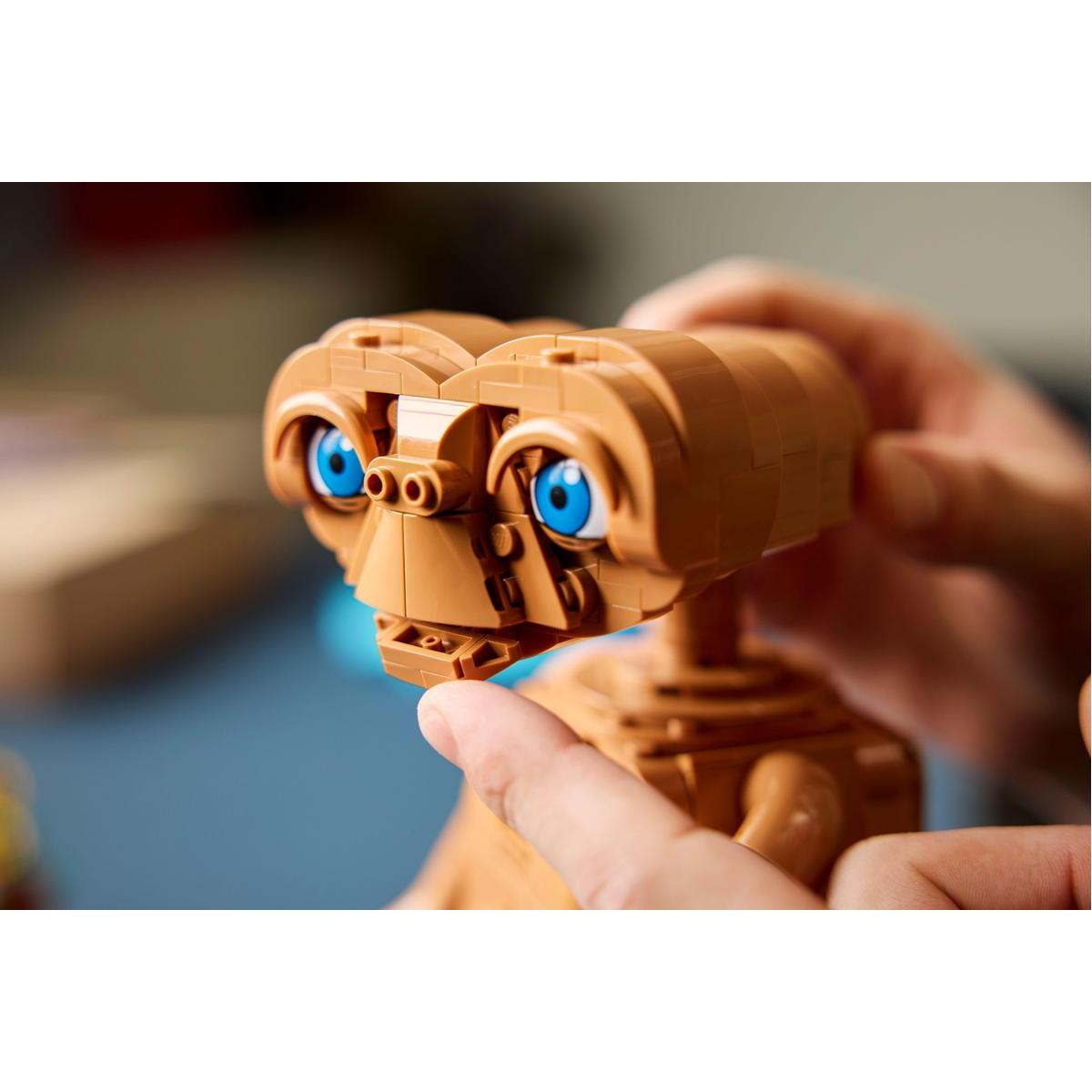 Primer plano de manos construyendo una figura de LEGO E.T. marrón con grandes ojos azules.