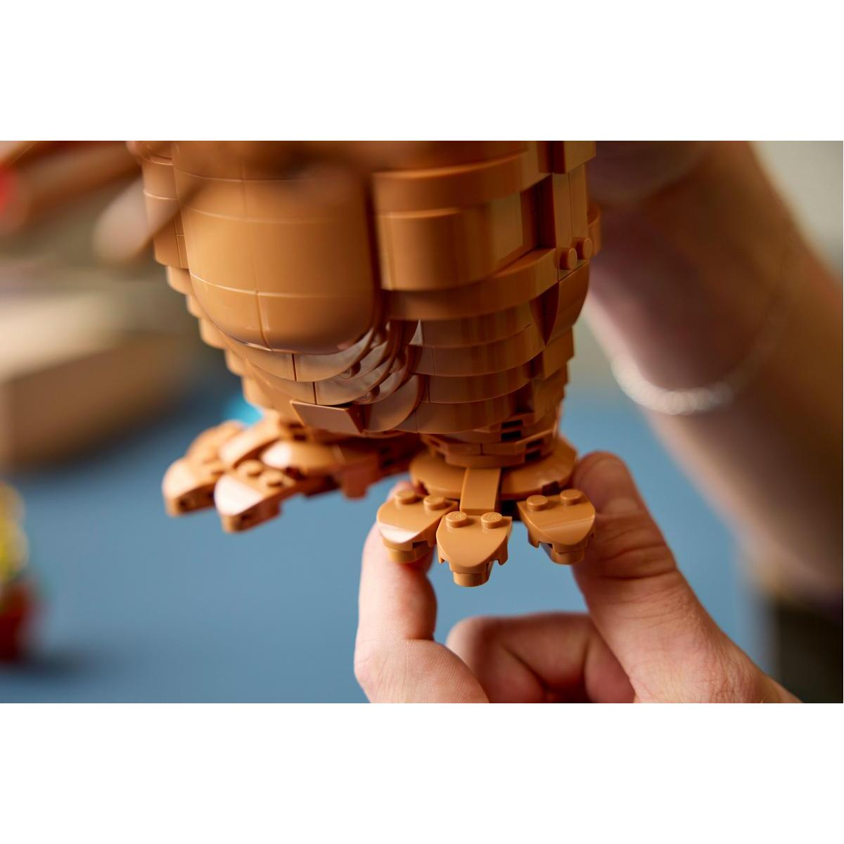 Manos sosteniendo los pies marrones y con garras de un modelo construido con piezas de Lego.