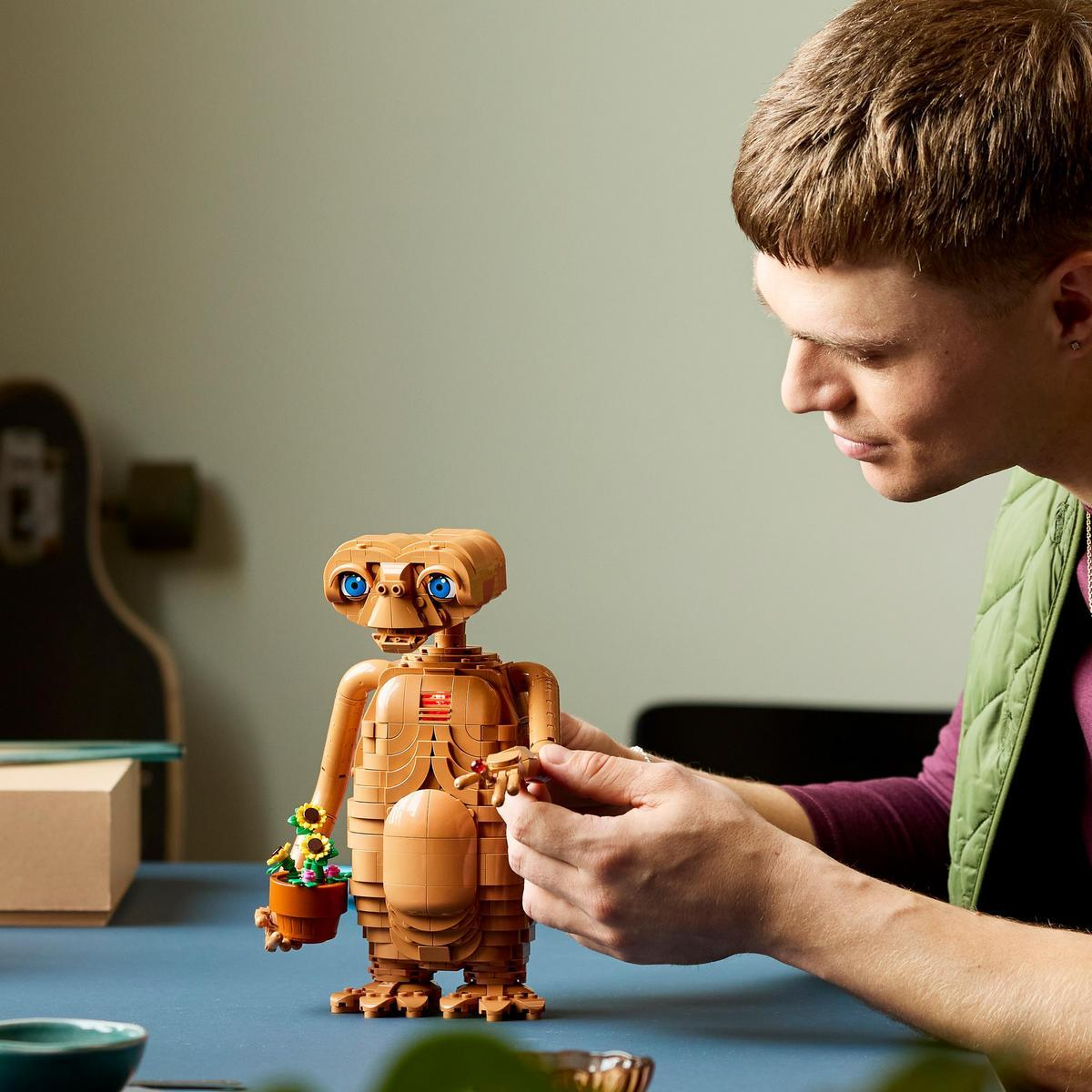 Un hombre construye una figura de LEGO de E.T. en una mesa azul.