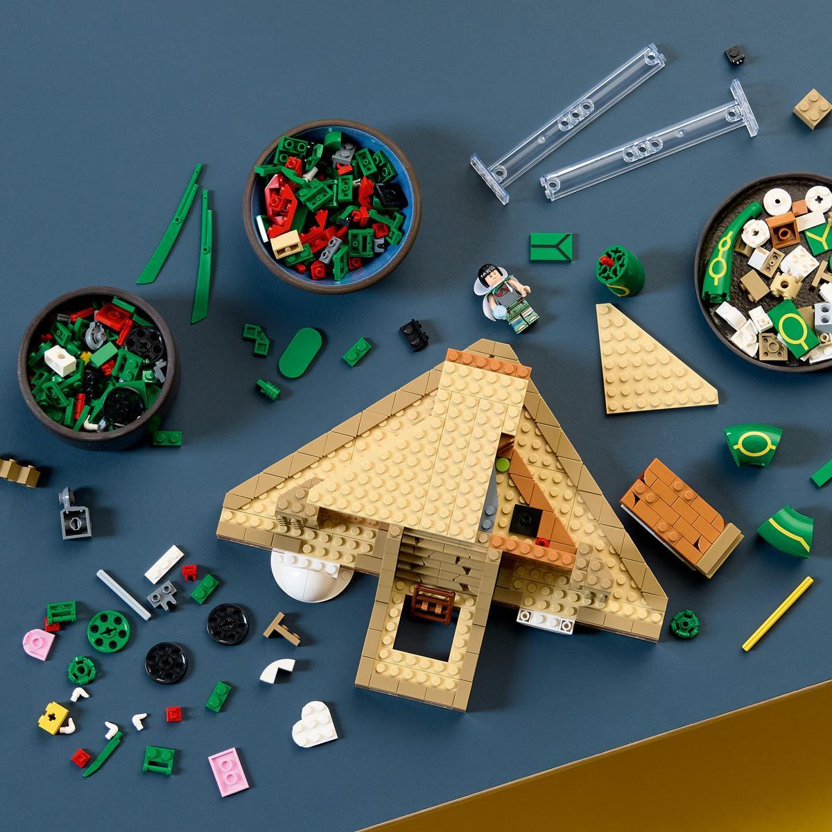 Mavi zemin üzerinde çeşitli Lego parçaları, renkli tuğlalarla dolu iki kase ve kısmi bir bina.