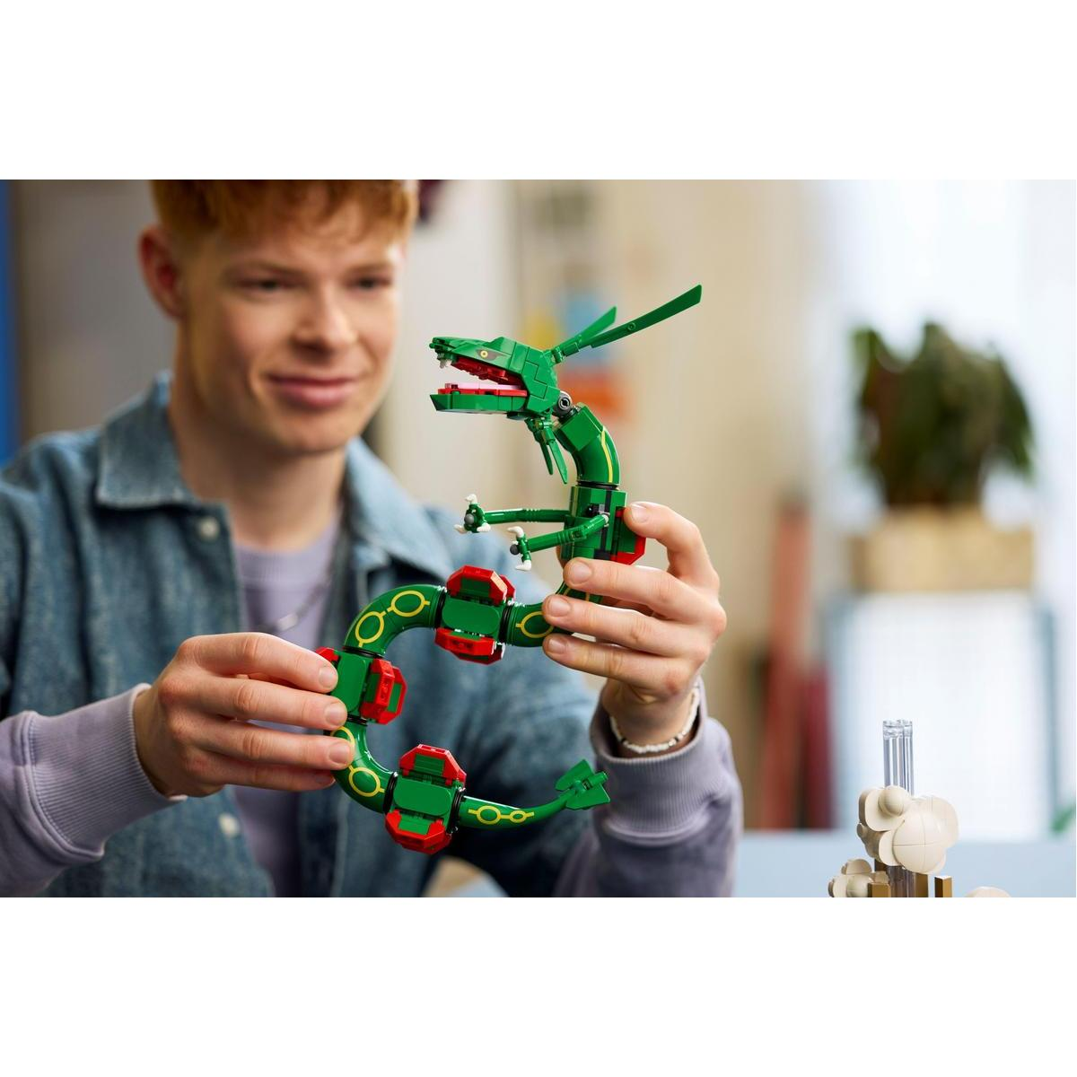 Genç bir adam içeride yeşil ve kırmızı bir Lego yılan figürünü tutarken gülümsüyor.