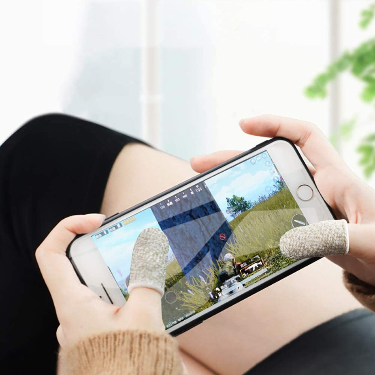 Una persona che gioca con lo smartphone, con copriditi da gaming sui pollici.