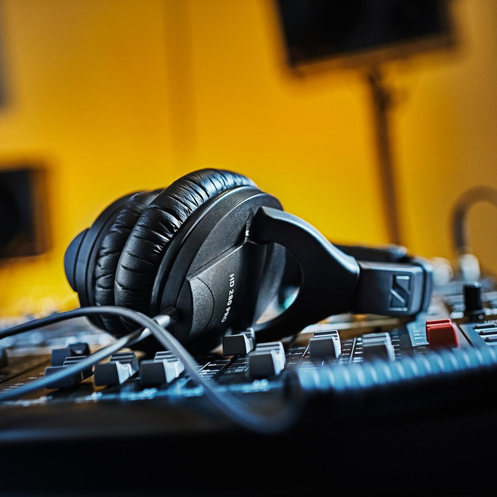 Auriculares negros descansan sobre una mesa de mezclas con fondo amarillo.