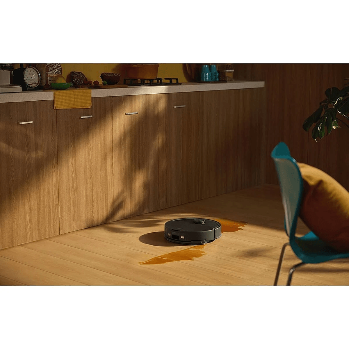 Un robot aspirapolvere scuro pulisce del liquido su un pavimento in legno vicino a dei mobili.