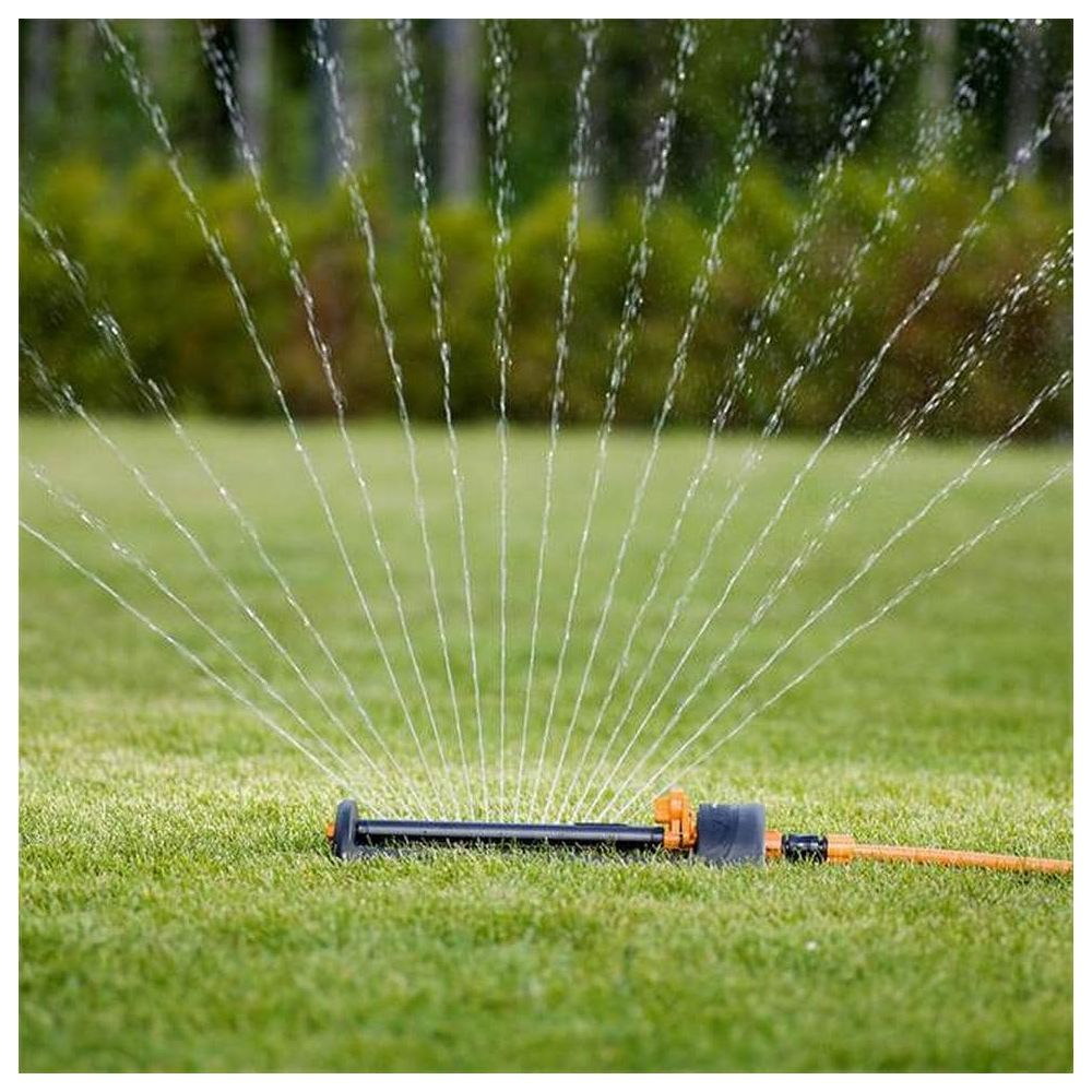Un irrigatore da giardino spruzza getti d'acqua ad arco su un prato verde con sfondo sfocato.