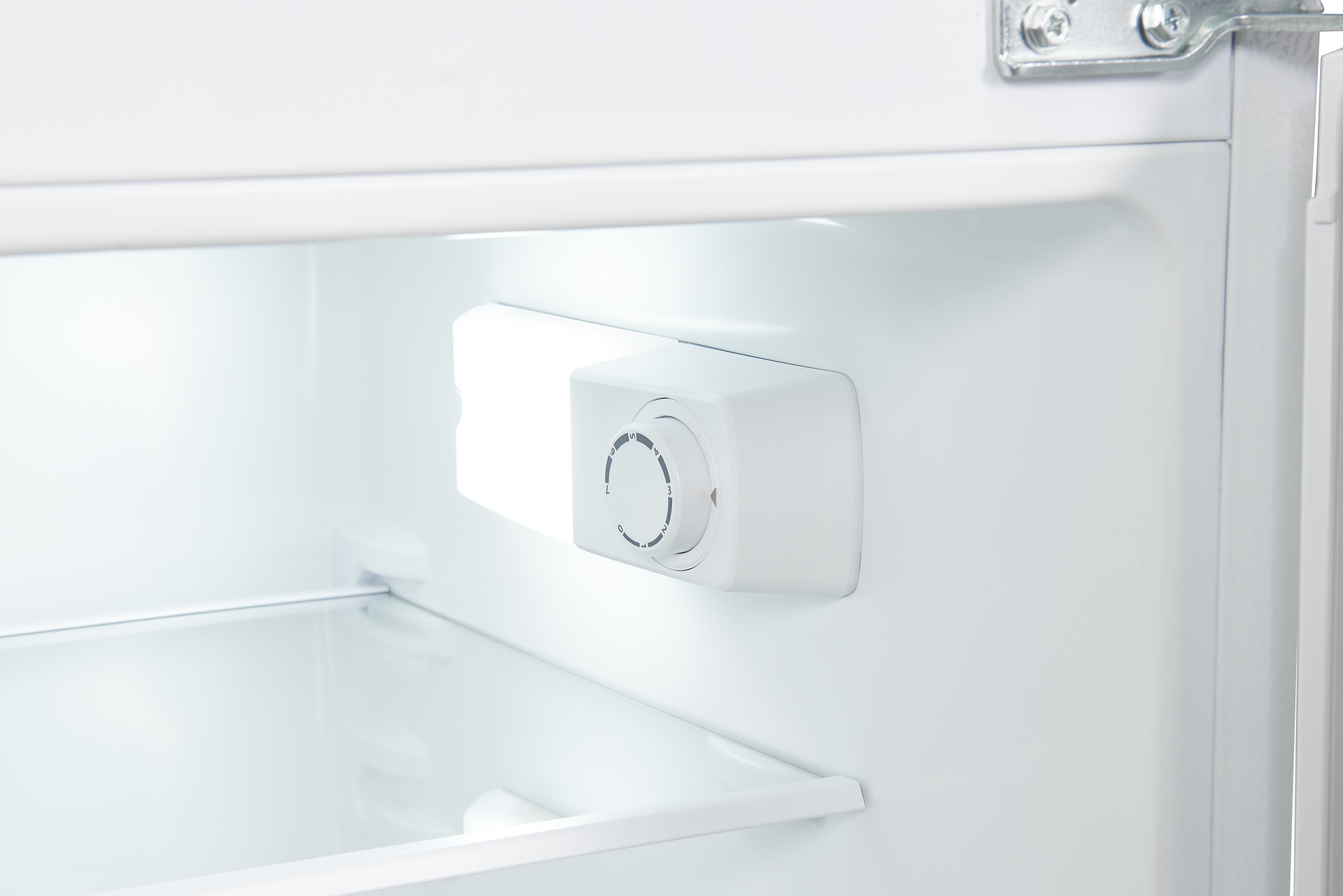 Vista interior de un refrigerador blanco con dial de control de temperatura junto a un estante de vidrio.
