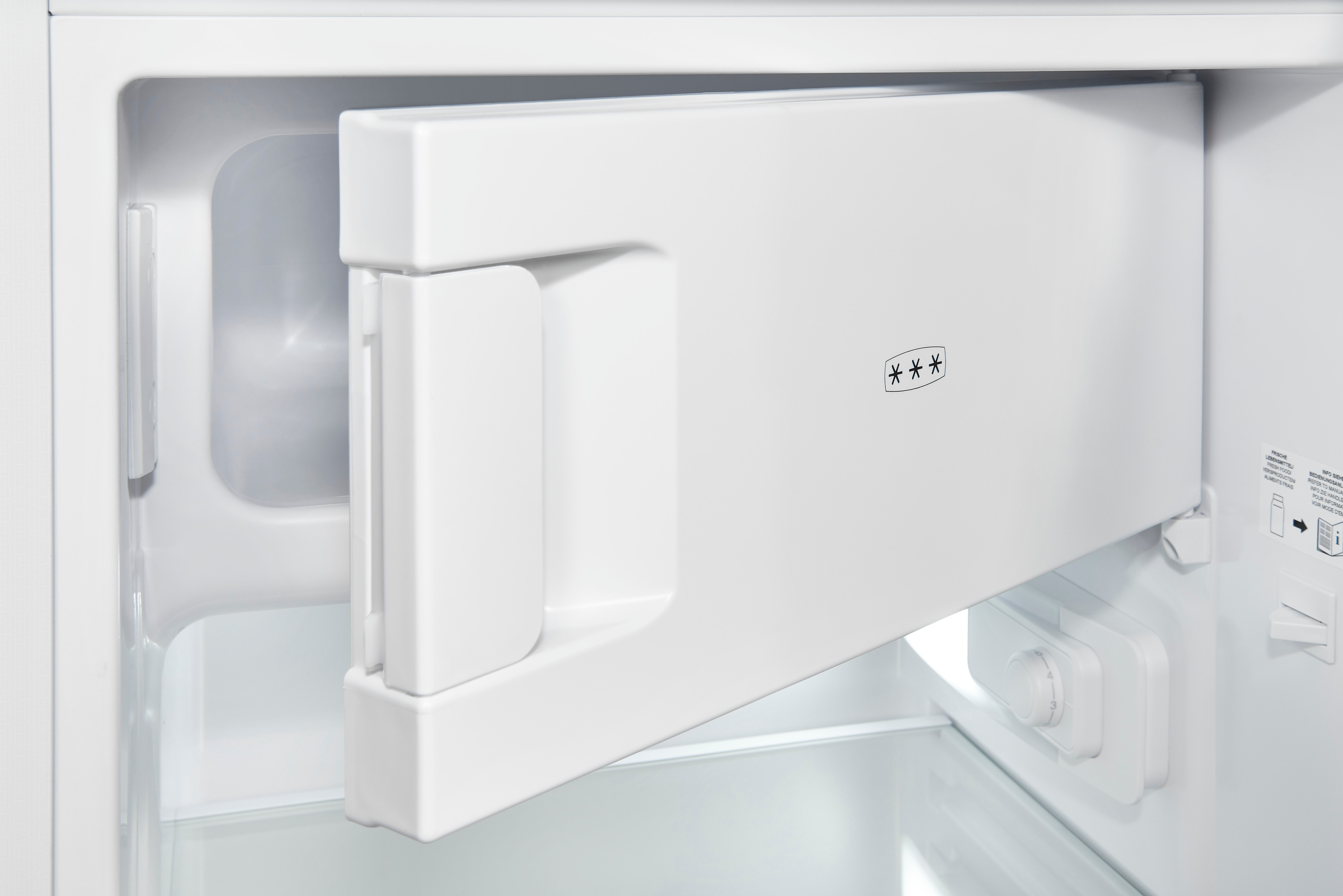 El compartimento congelador pequeño abierto de un refrigerador blanco con control de temperatura y estante.