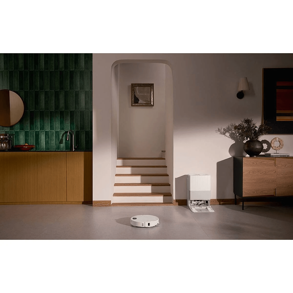 Un robot aspirapolvere bianco sul pavimento in un corridoio moderno con scale e mobili.