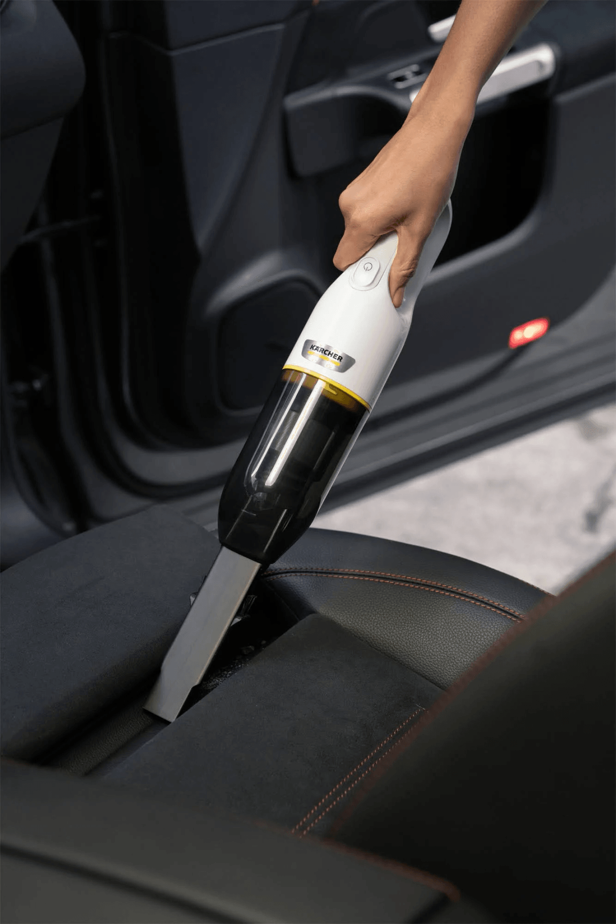 Una mano usa un aspirapolvere portatile senza fili per pulire il sedile dell'auto.