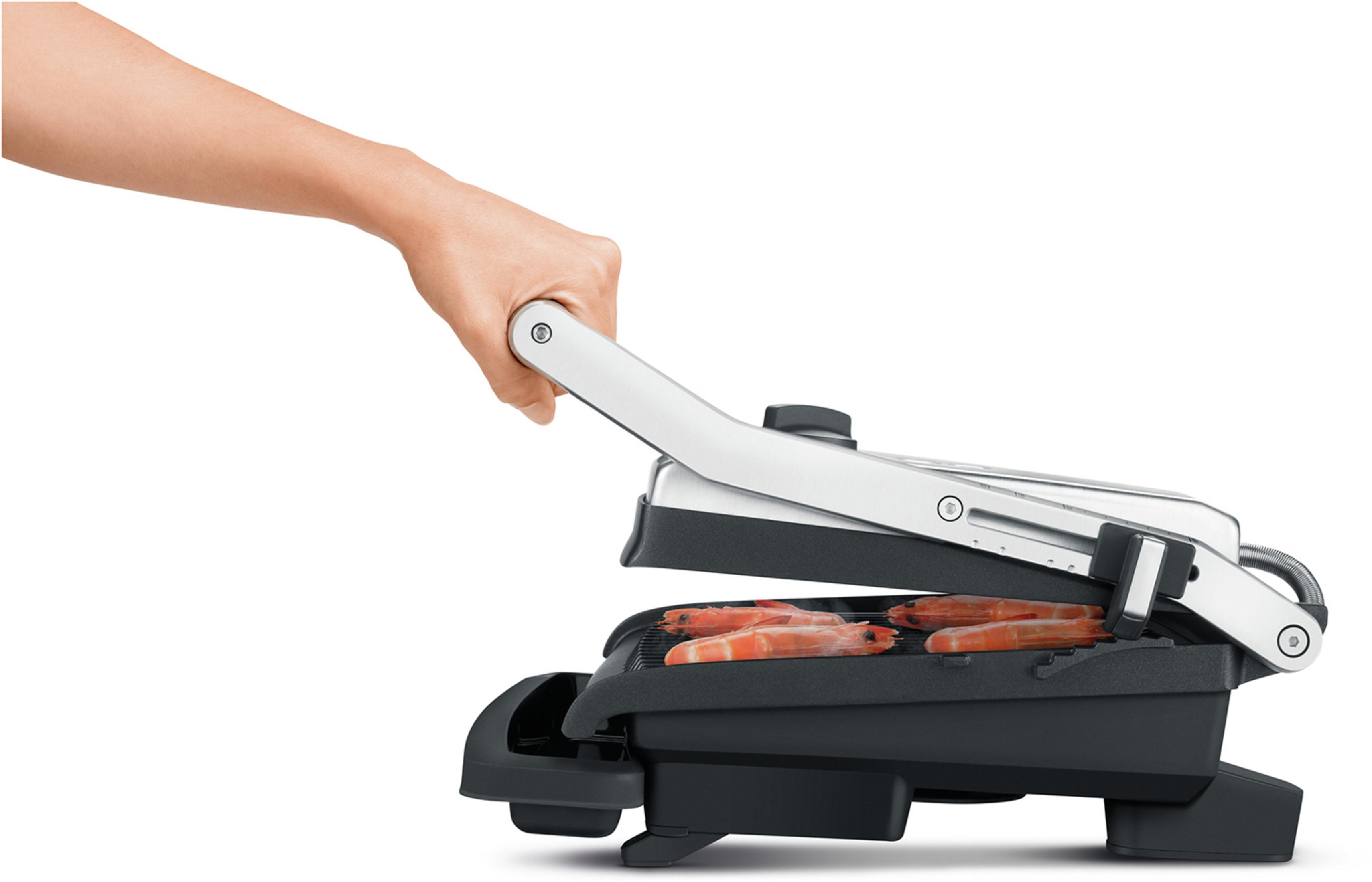Eine Hand öffnet einen schwarzen Kontaktgrill mit silbernem Griff, auf dem Garnelen grillen.