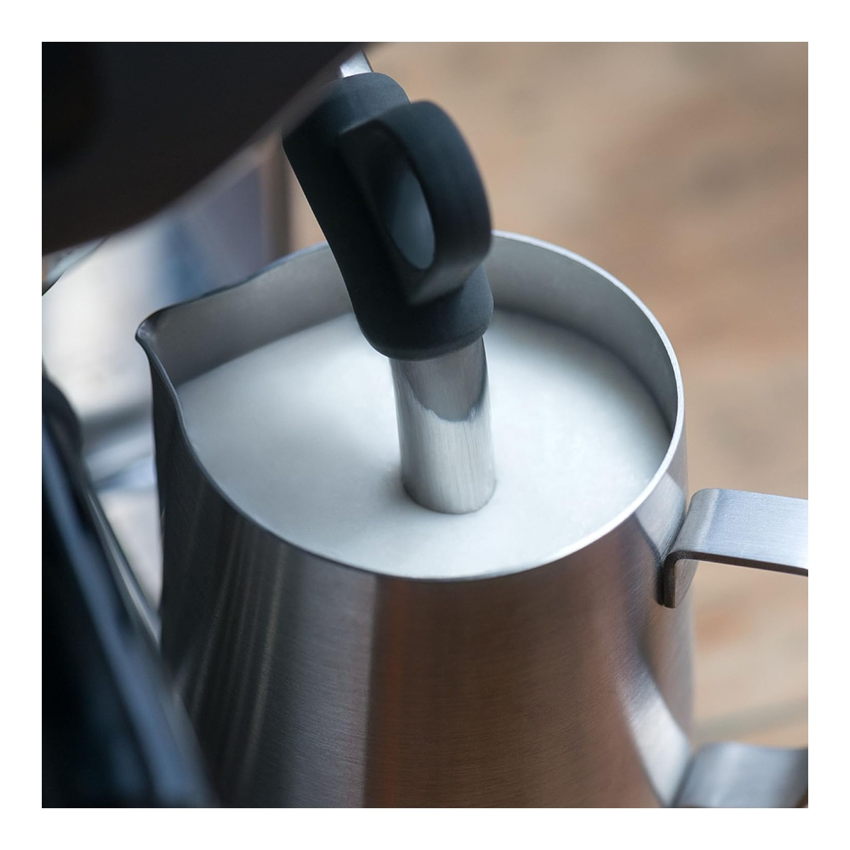 Een stoompijpje schuimt melk op in een roestvrijstalen melkkan.