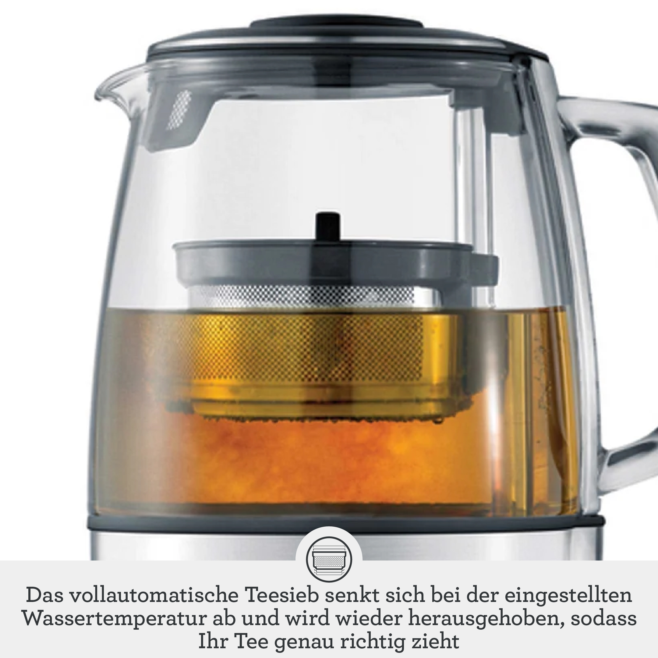 Una tetera de vidrio con colador de metal y té ámbar, sobre una base gris con texto en alemán.