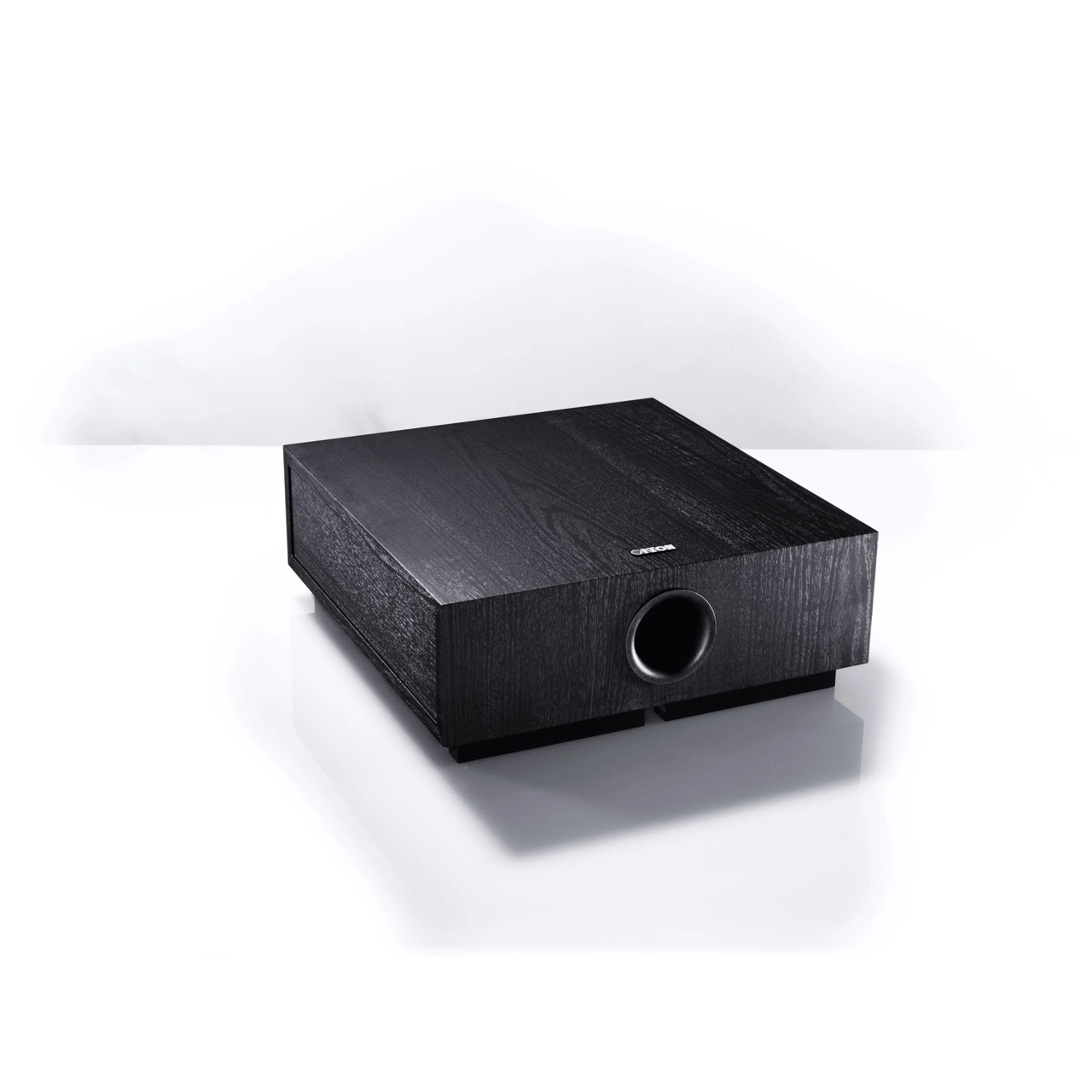 Ein schwarzer Canton-Subwoofer aus Holz steht auf einer weißen reflektierenden Oberfläche vor weißem Hintergrund.