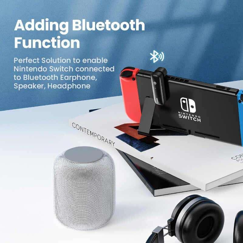 Kitaplar üzerinde Bluetooth adaptörlü Nintendo Switch, yuvarlak bir hoparlör ve kulaklığın yanında.