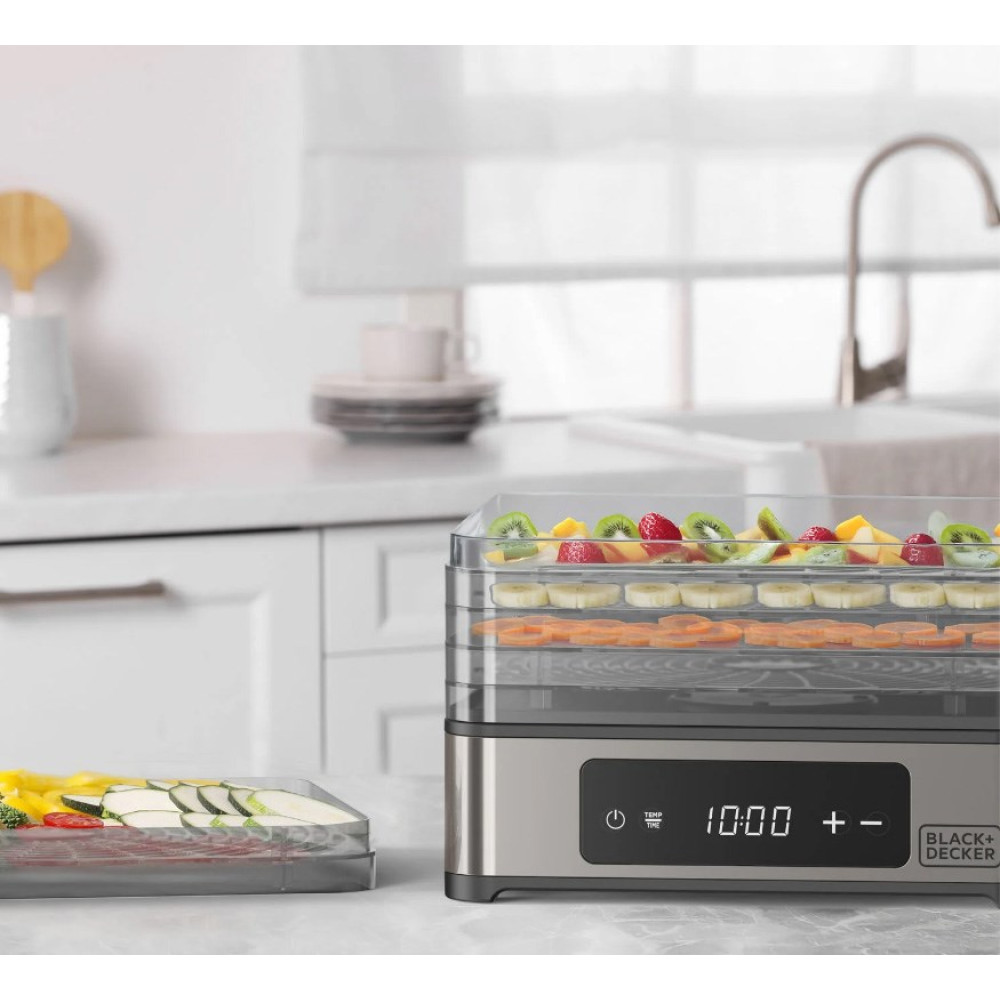 Czarna suszarka do żywności Black+Decker stoi na blacie kuchennym z tacami jedzenia.