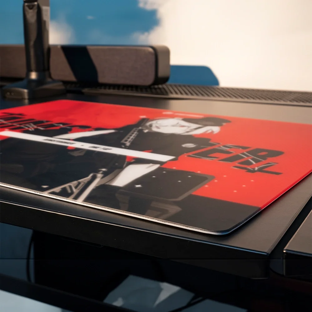 Siyah ve kırmızı bir oyuncu mousepad'i, arka planda hoparlör ve stant olan bir masada duruyor.