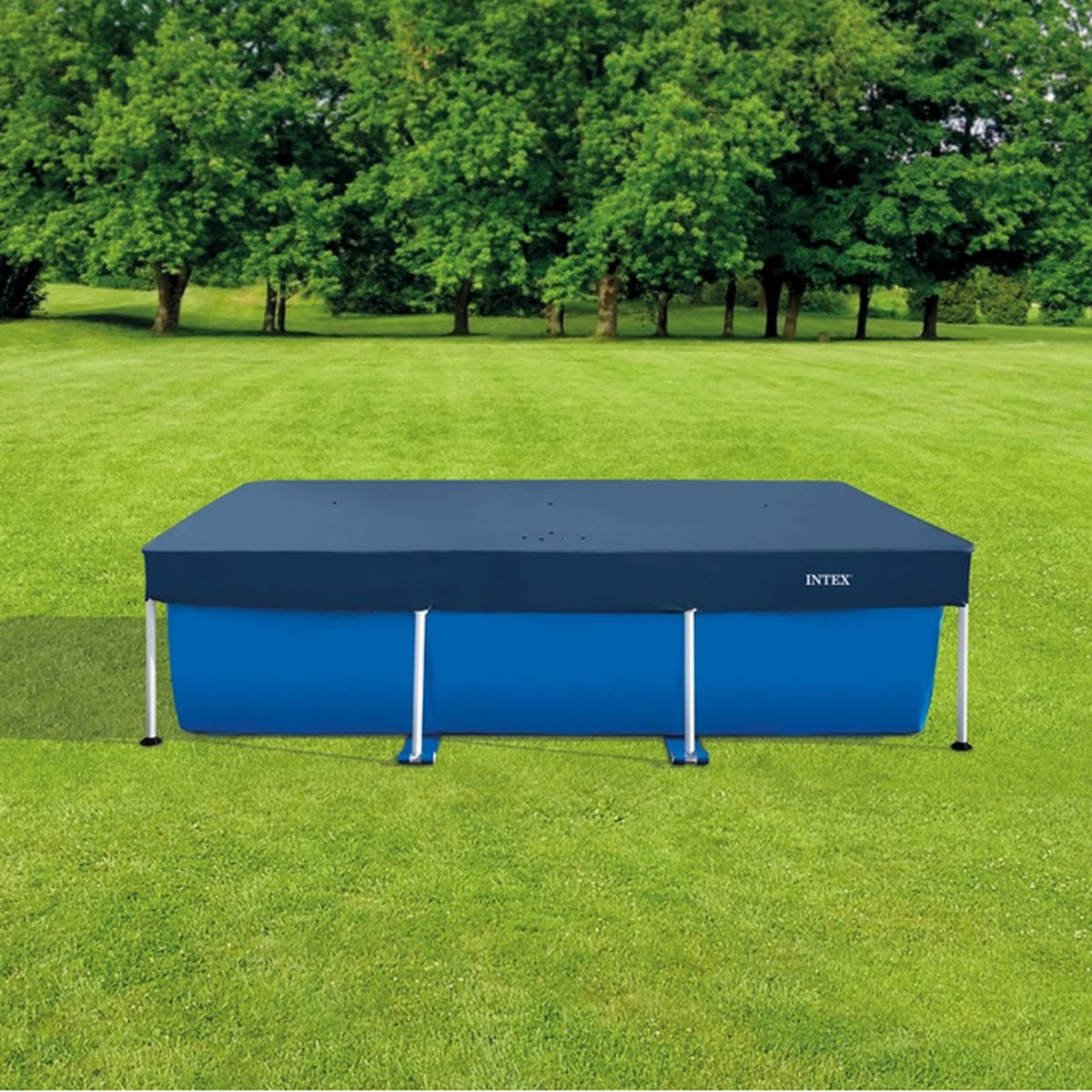 Ein blauer rechteckiger Aufstellpool mit einer dunklen Abdeckung steht auf einer grünen Rasenfläche vor Bäumen.