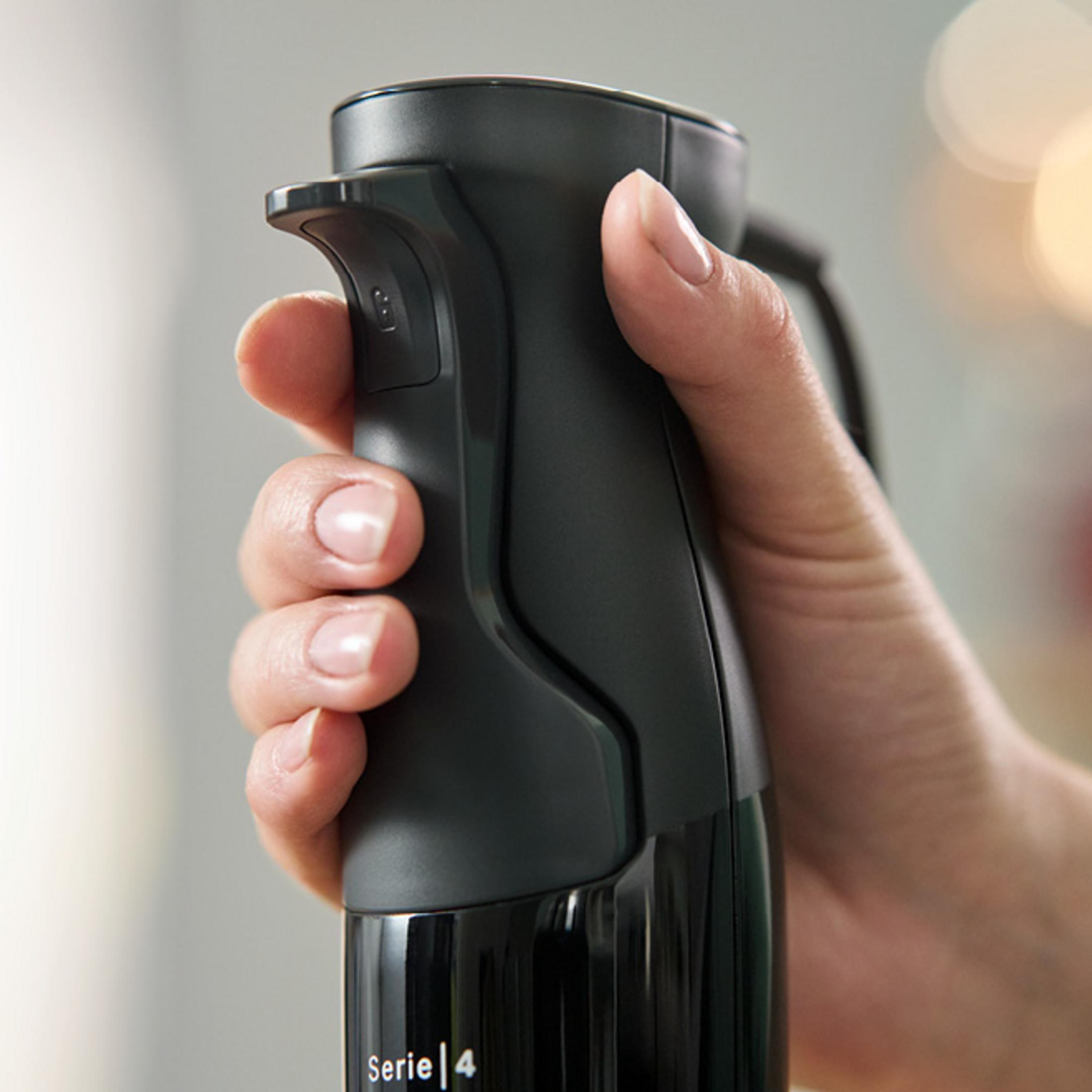 Eine Hand hält den schwarzen Griff eines Bosch Serie 4 Stabmixers vor verschwommenem Hintergrund.