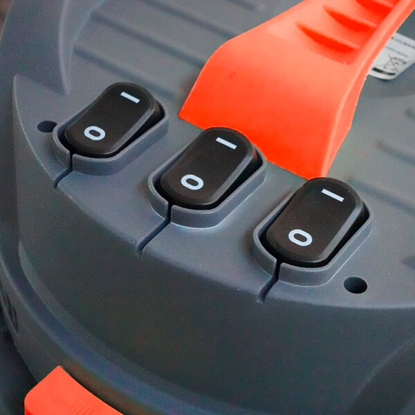 Tres interruptores basculantes negros con símbolos blancos de encendido y apagado en una máquina gris con asa naranja.