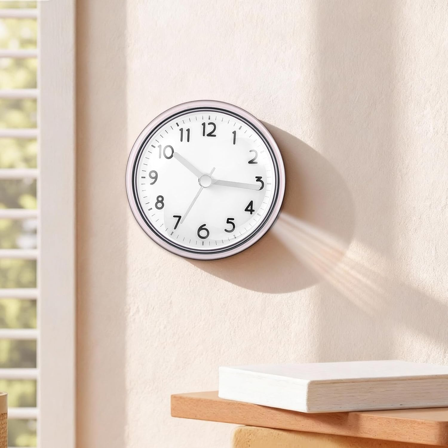 Eine runde, weiße Uhr mit schwarzen Zahlen hängt an einer beigen Wand neben einem Holzregal.