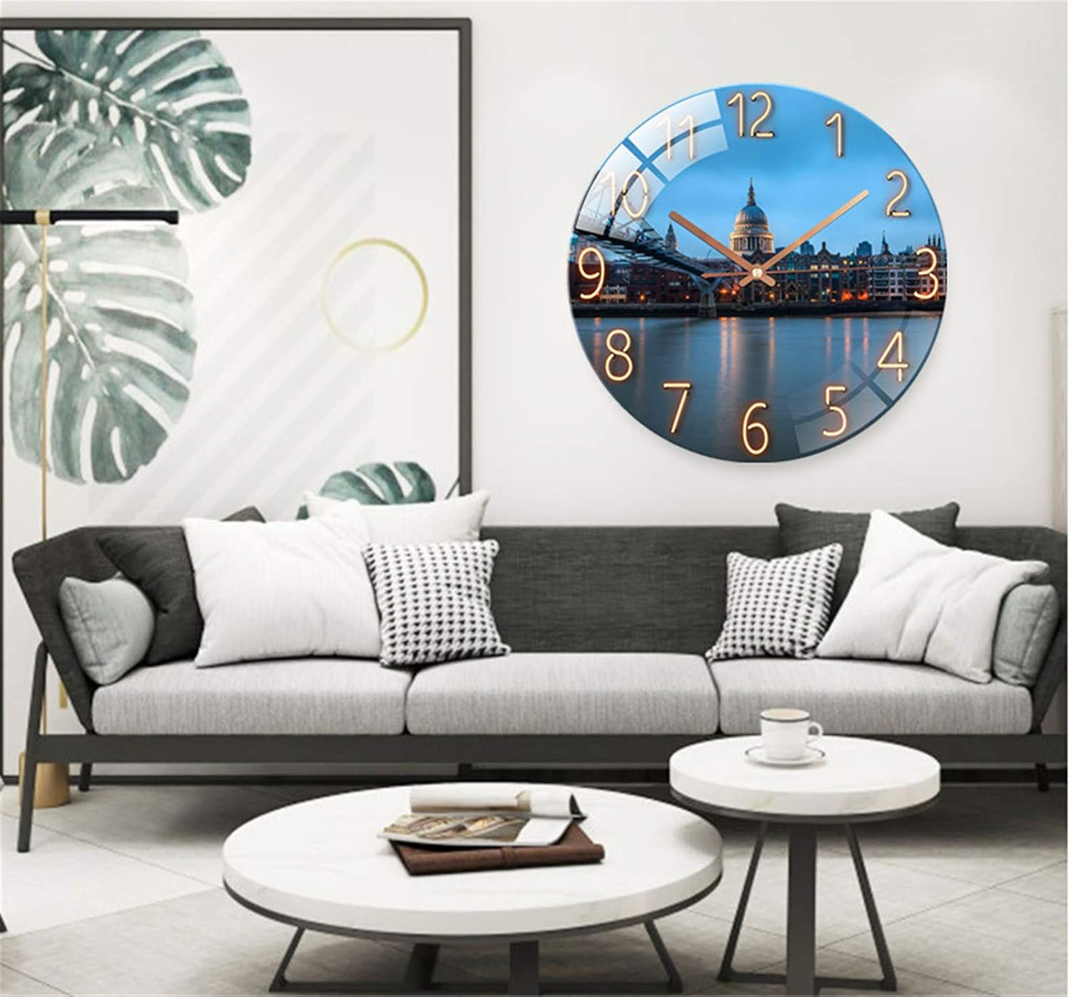 Ein modernes Wohnzimmer mit grauem Sofa, weißen Tischen, Blatt-Wandkunst und einer Londoner Skyline-Uhr.