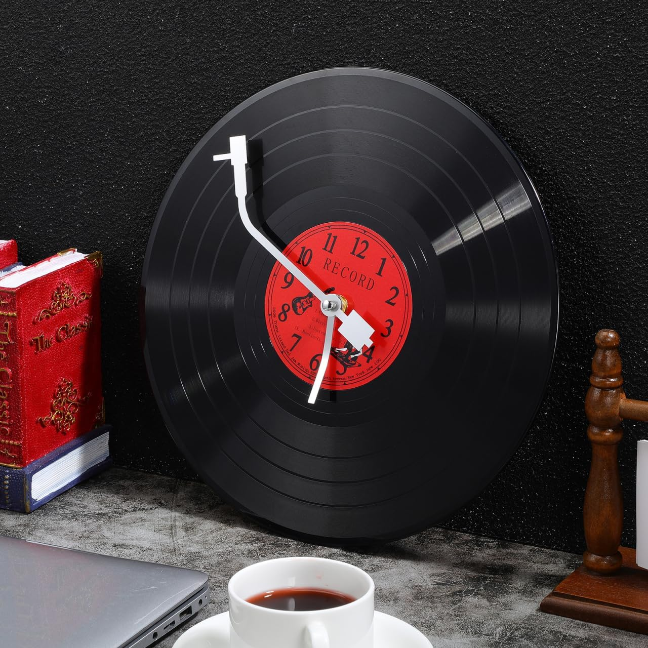 Wanduhr im Vinylplatten-Design mit rotem Zentrum und weißen Zeigern vor einer dunklen Wand.