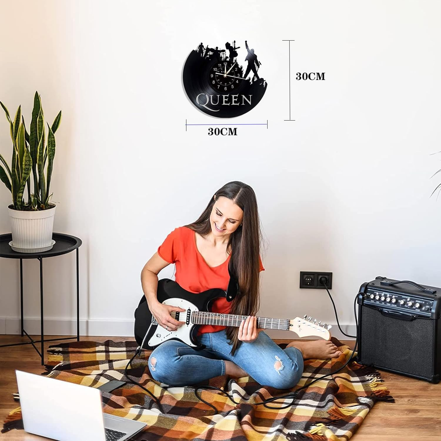 Eine Frau spielt E-Gitarre auf einer Decke, an der Wand hängt eine Queen-Uhr.