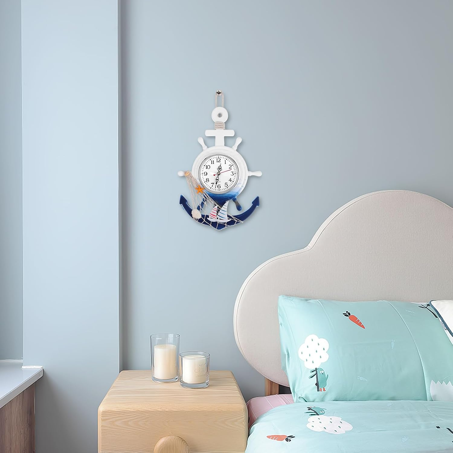Ein ankerformiges Wanduhr hängt über einem Nachttisch mit Kerzen neben einem grauen Bett.