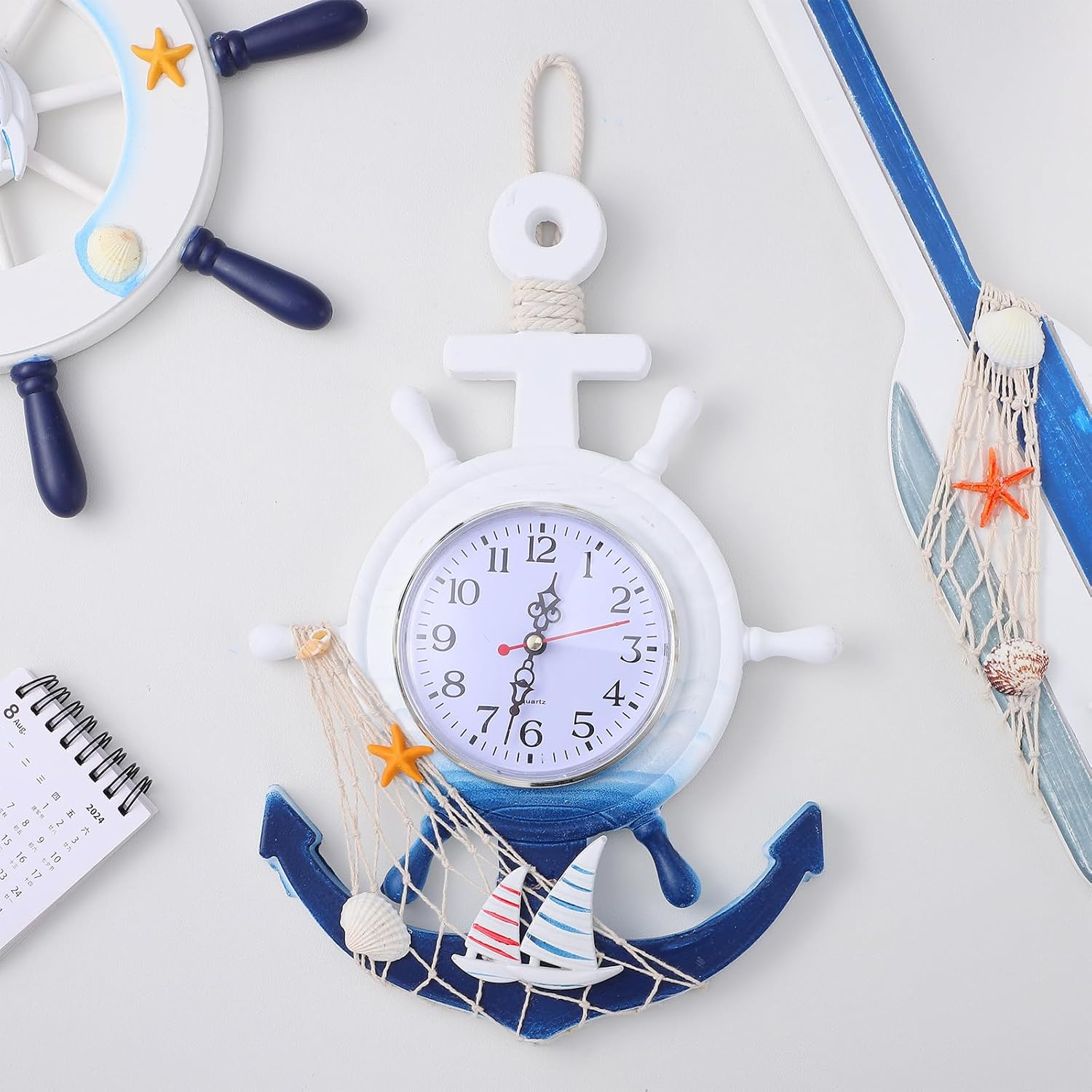 Eine maritime Wanduhr im Schiffsanker-Design mit Segelbooten, Netz und Muscheln.